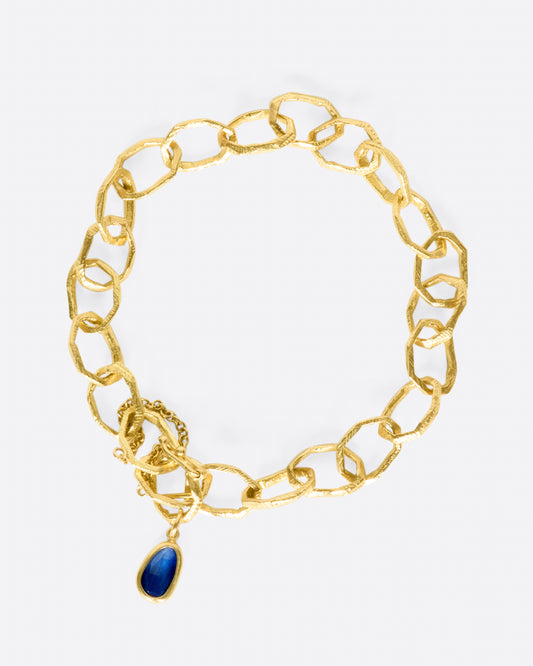 Each large link on this chain bracelet is hand carved, as is the bezel setting of its deep blue sapphire charm.