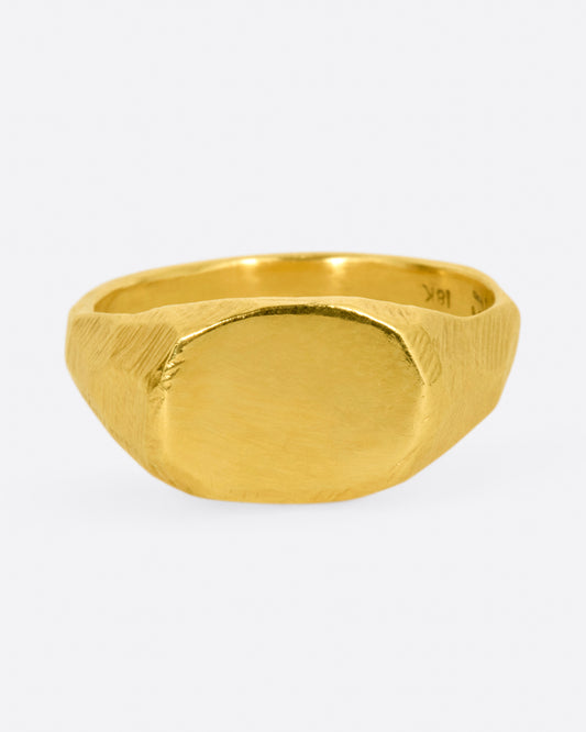 A yellow gold signet ring with a flat, polished face and textured band. Shown from the side.