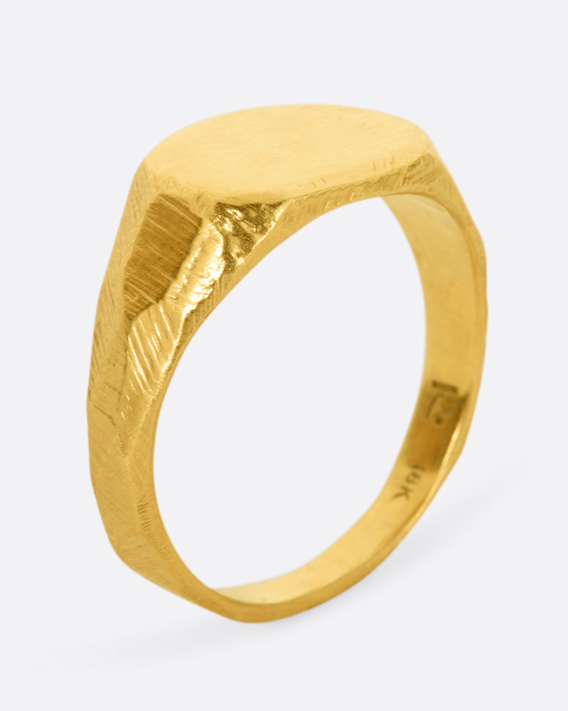 A yellow gold signet ring with a flat, polished face and textured band. Shown from the side.