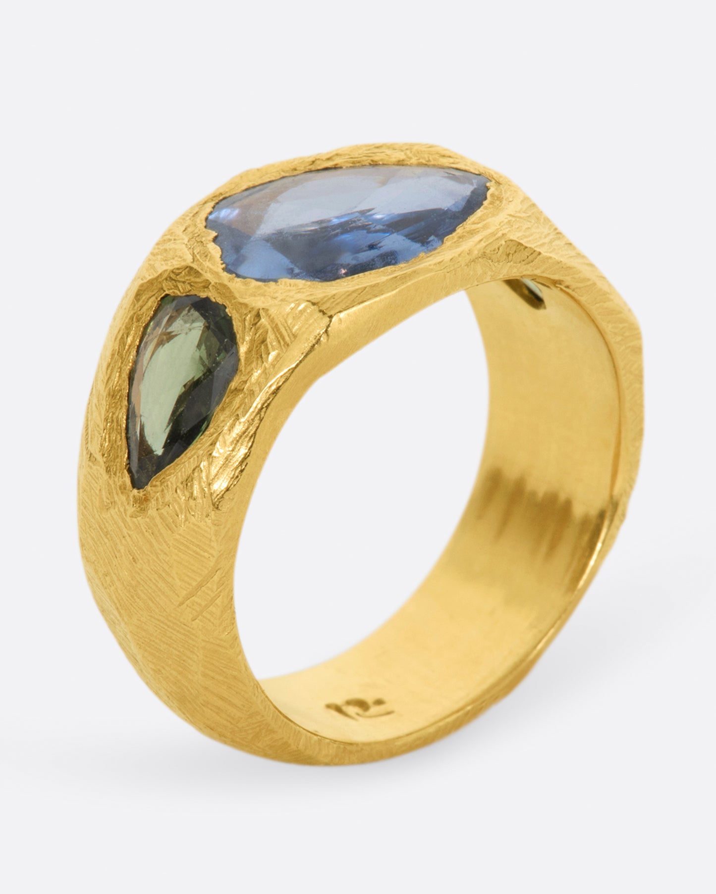 A brushed texture yellow gold ring with a large rose cut blue sapphire at its center with one green pear shaped sapphire on either side. Shown from the side.