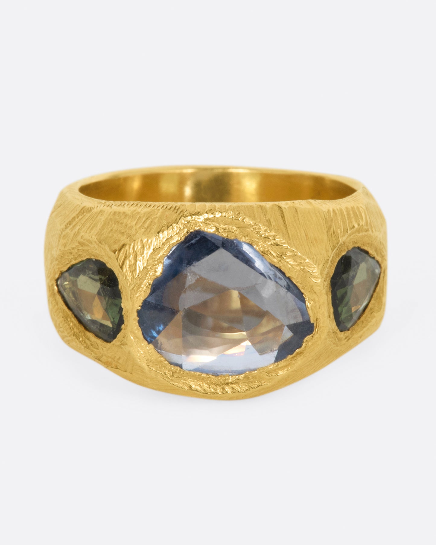 A brushed texture yellow gold ring with a large rose cut blue sapphire at its center with one green pear shaped sapphire on either side. 