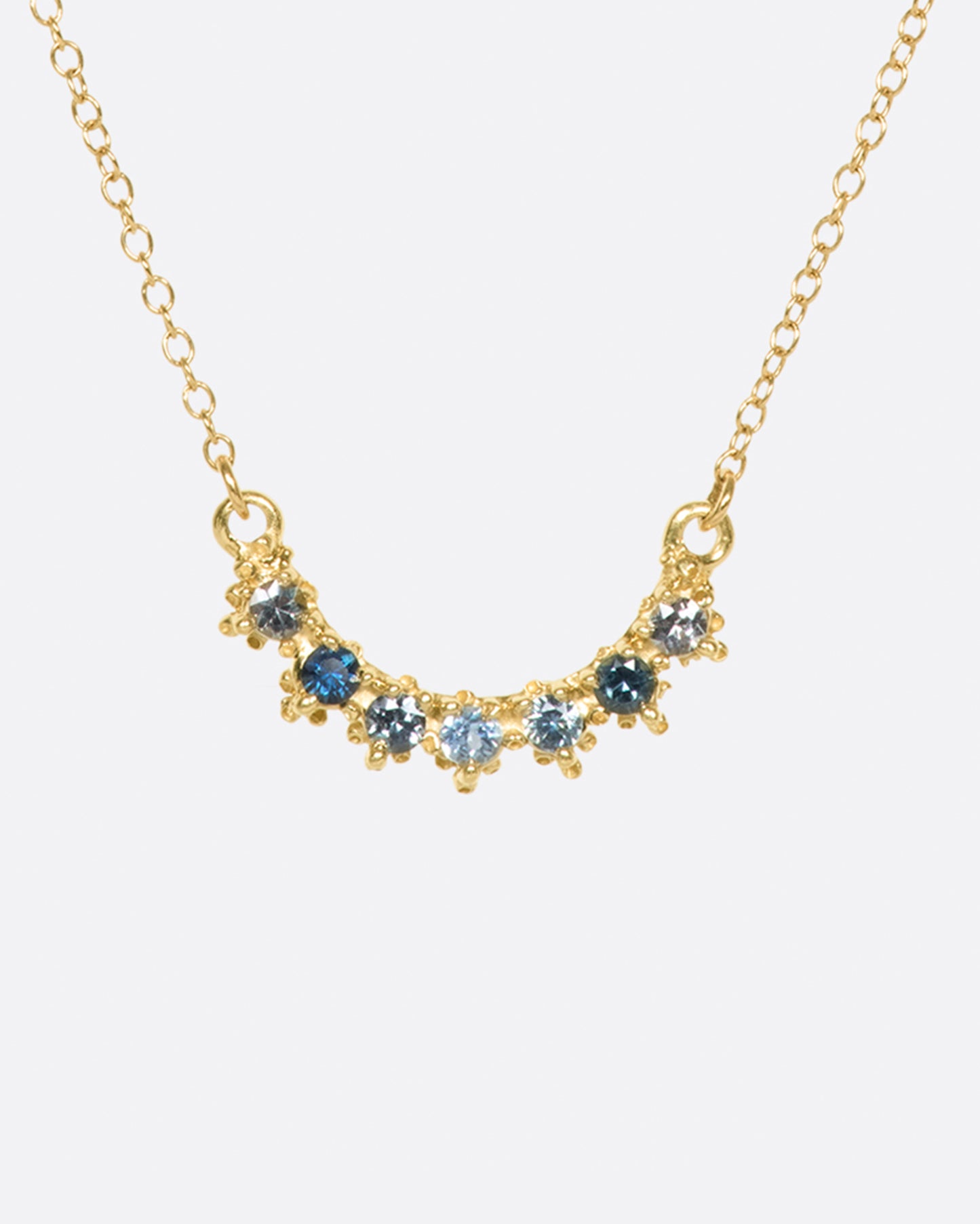 A curved bar necklace set with seven sapphires in varying shades of blue.