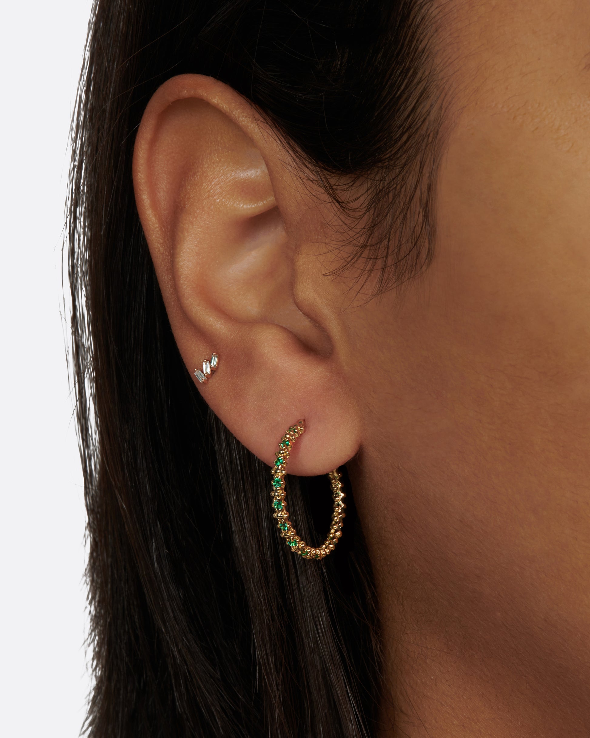 A pair of textured hoop earrings with emeralds dotted throughout.