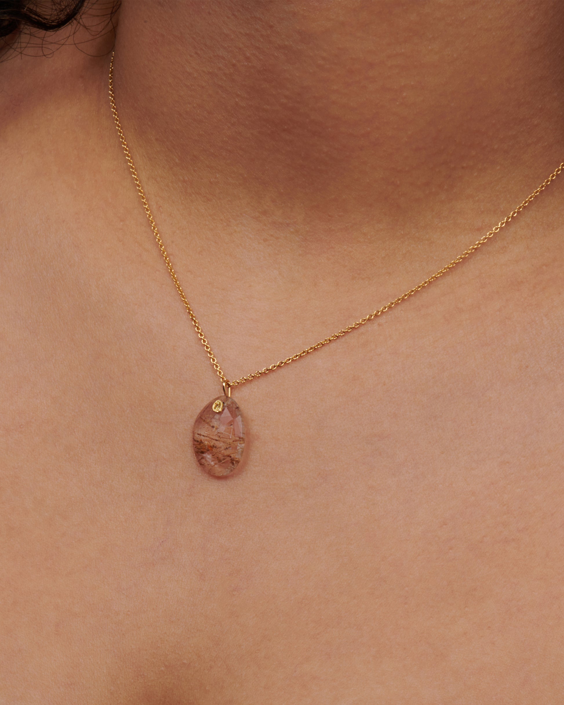 A yellow gold charm featuring a slice of rutilated quartz, with a yellow sapphire at its center. Shown on a neck.