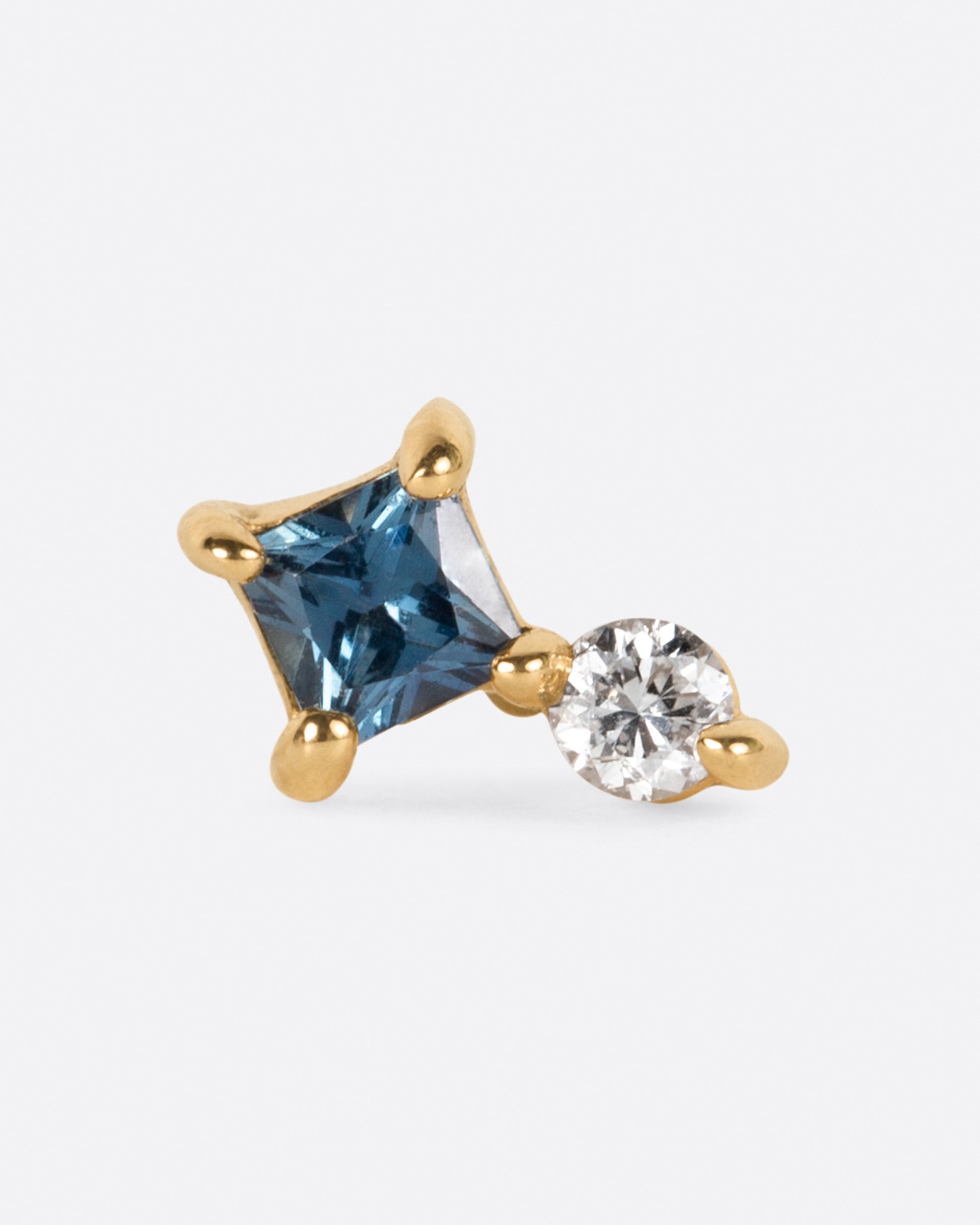 A prong set round diamond sitting atop a princess cut teal blue sapphire.