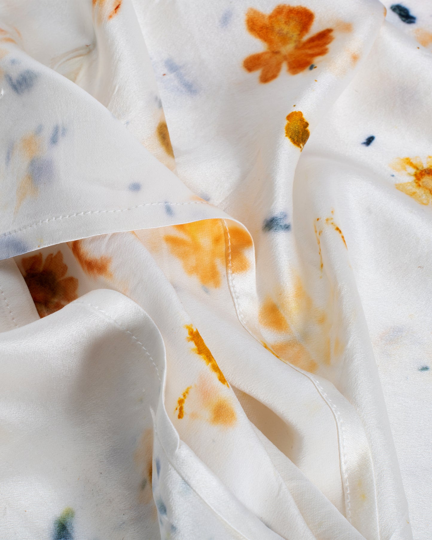 A close up of a yellow and orange flower dotted silk pillowcase.