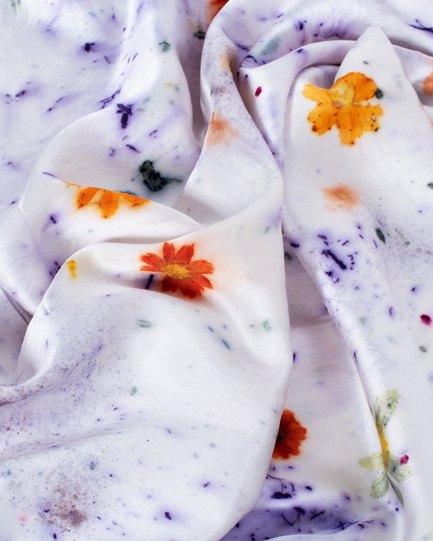 A close up of a purple and orange flower dotted silk pillowcase.