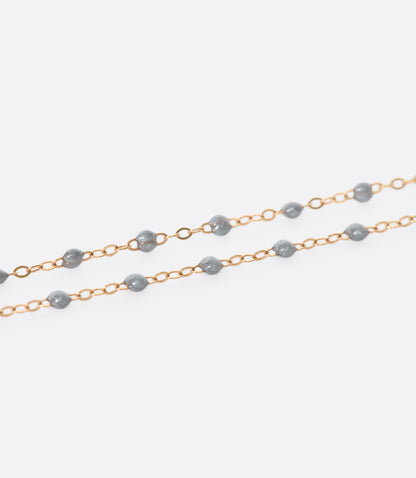 A close up view of a yellow gold cable chain necklace with silver resin droplets. Shown from the side.