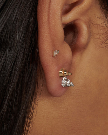 A white gold conical stud earring, with diamond accents, shown on an ear with a yellow gold conical stud earring and a diamond stud earring.