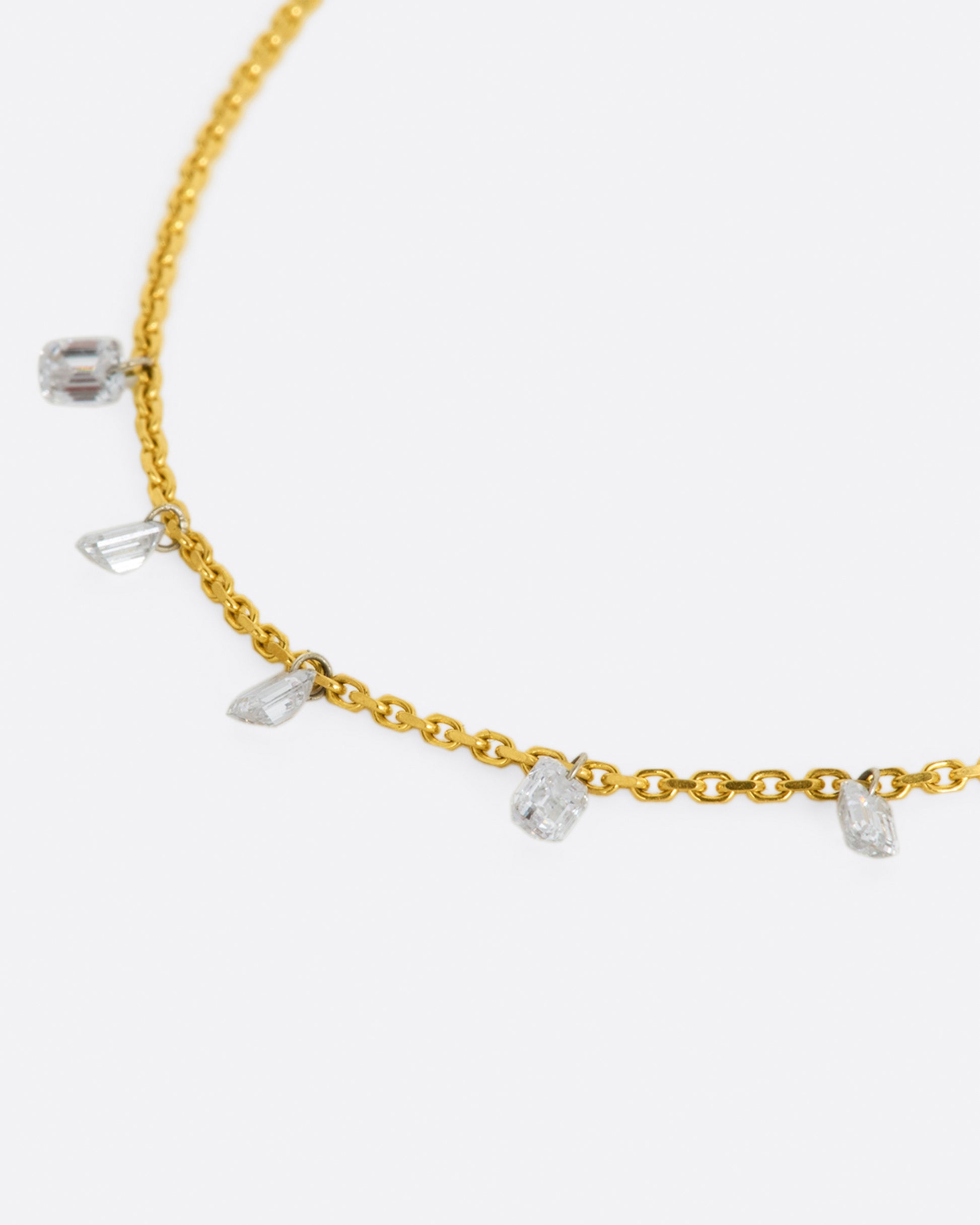 A yellow gold chain necklace with five free set dangling emerald cut diamonds spaced about half an inch apart from one another. Shown from the side.