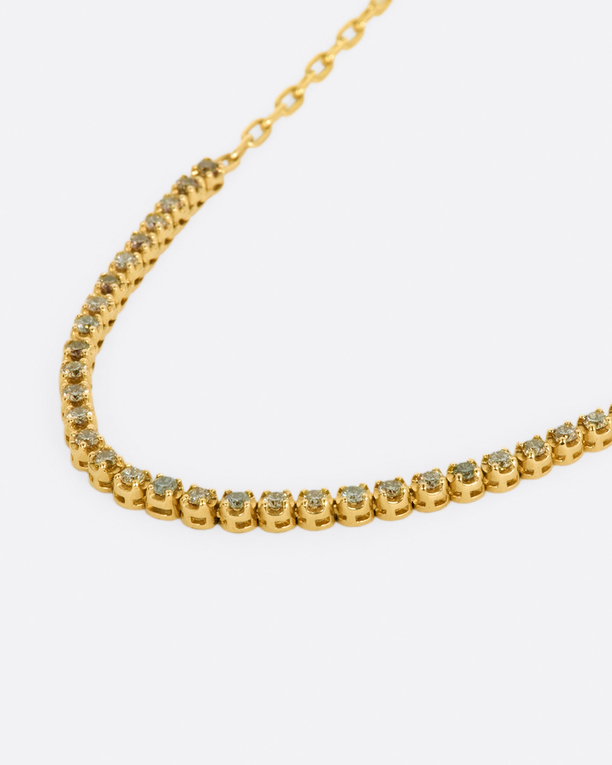 A yellow gold chain necklace with a section of green, champagne and cognac diamonds along the front. Shown from the side.