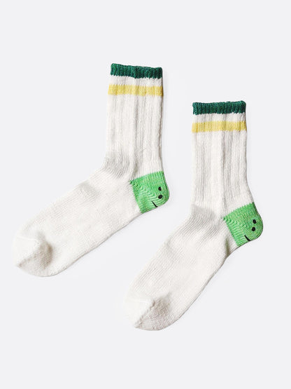 A pair of white socks with green smiley heels, and yellow and green stripes on each ankle. Shown from the side.