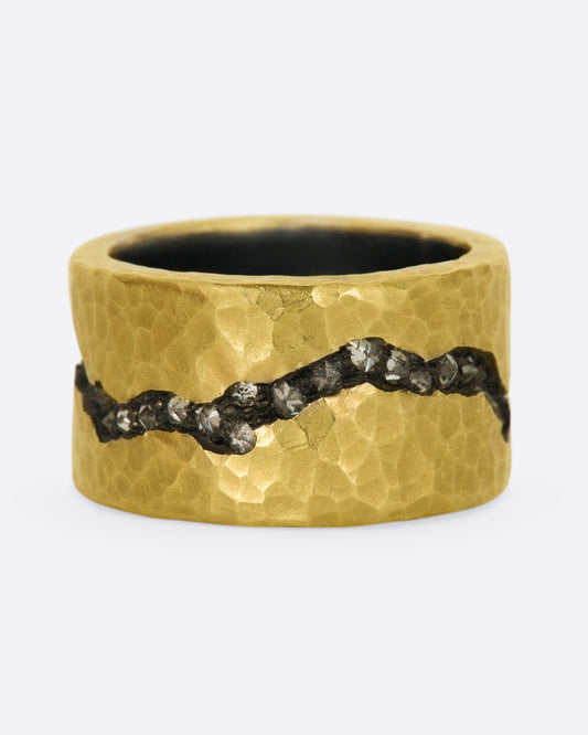 A wide sterling silver band ring with a layer of hammered 18k yellow gold on top and a fissure all the way around that's lined with inverted diamonds.