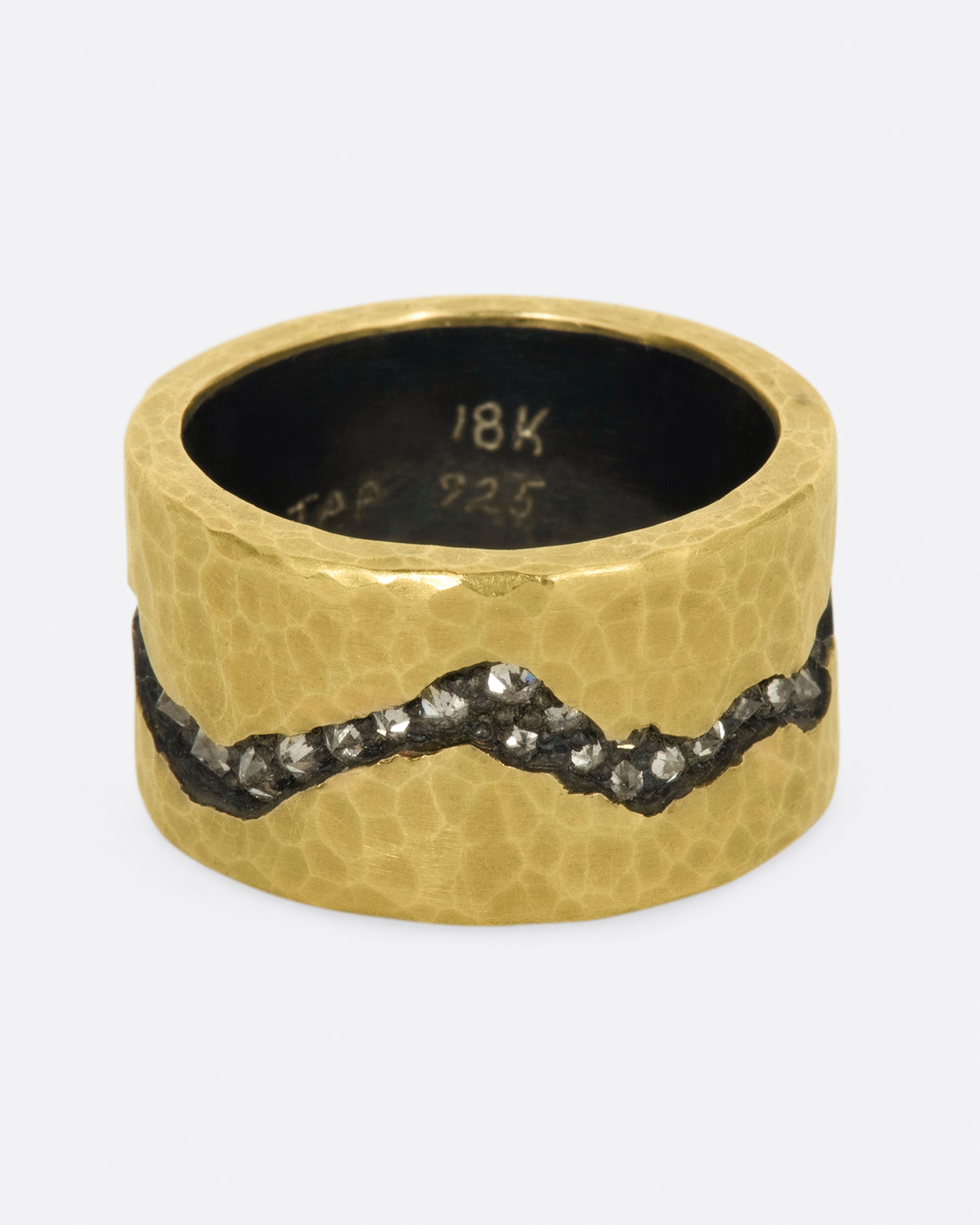 A wide sterling silver band ring with a layer of hammered 18k yellow gold on top and a fissure all the way around that's lined with inverted diamonds.