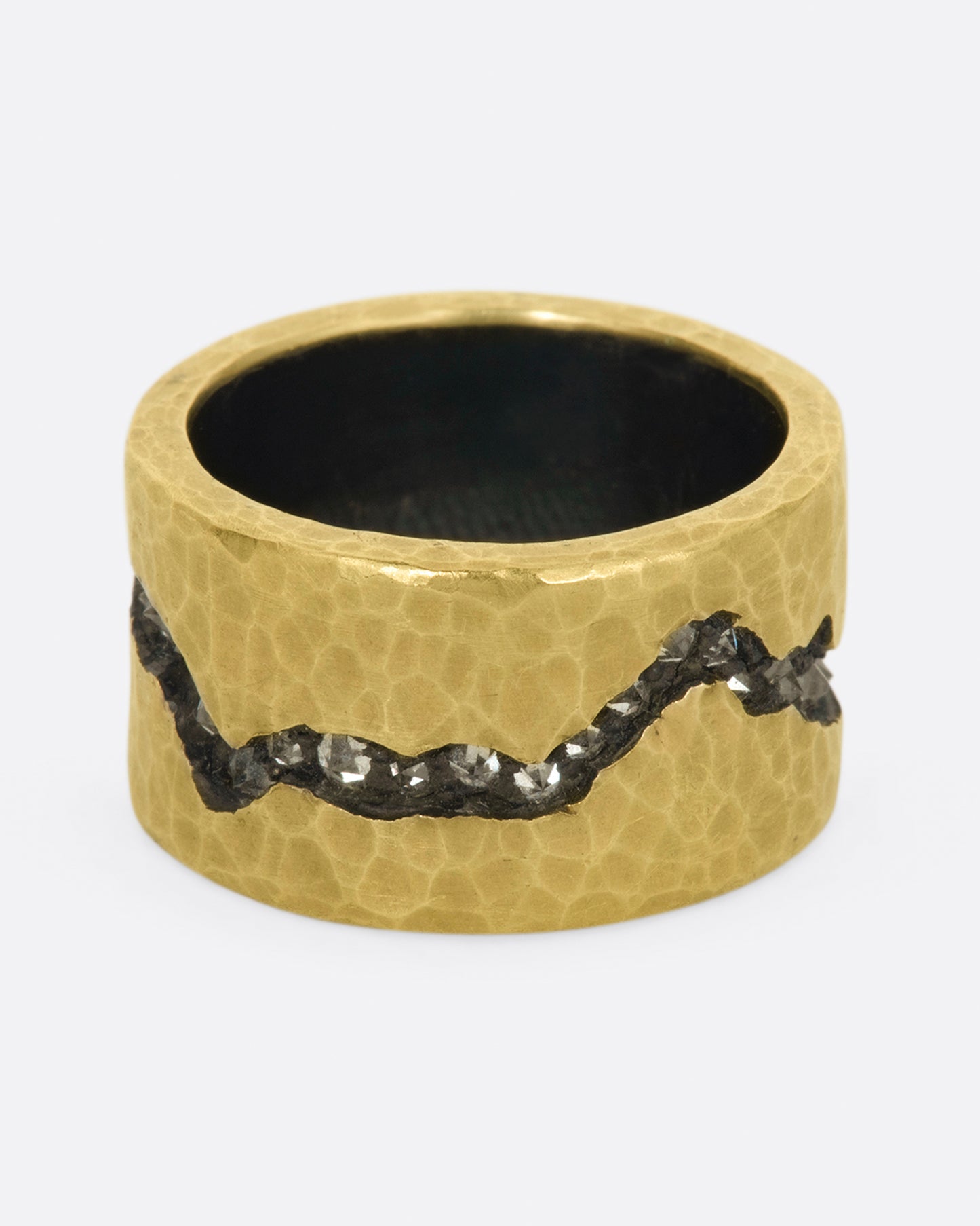 A wide sterling silver band ring with a layer of hammered 18k yellow gold on top and a fissure all the way around that's lined with inverted diamonds.