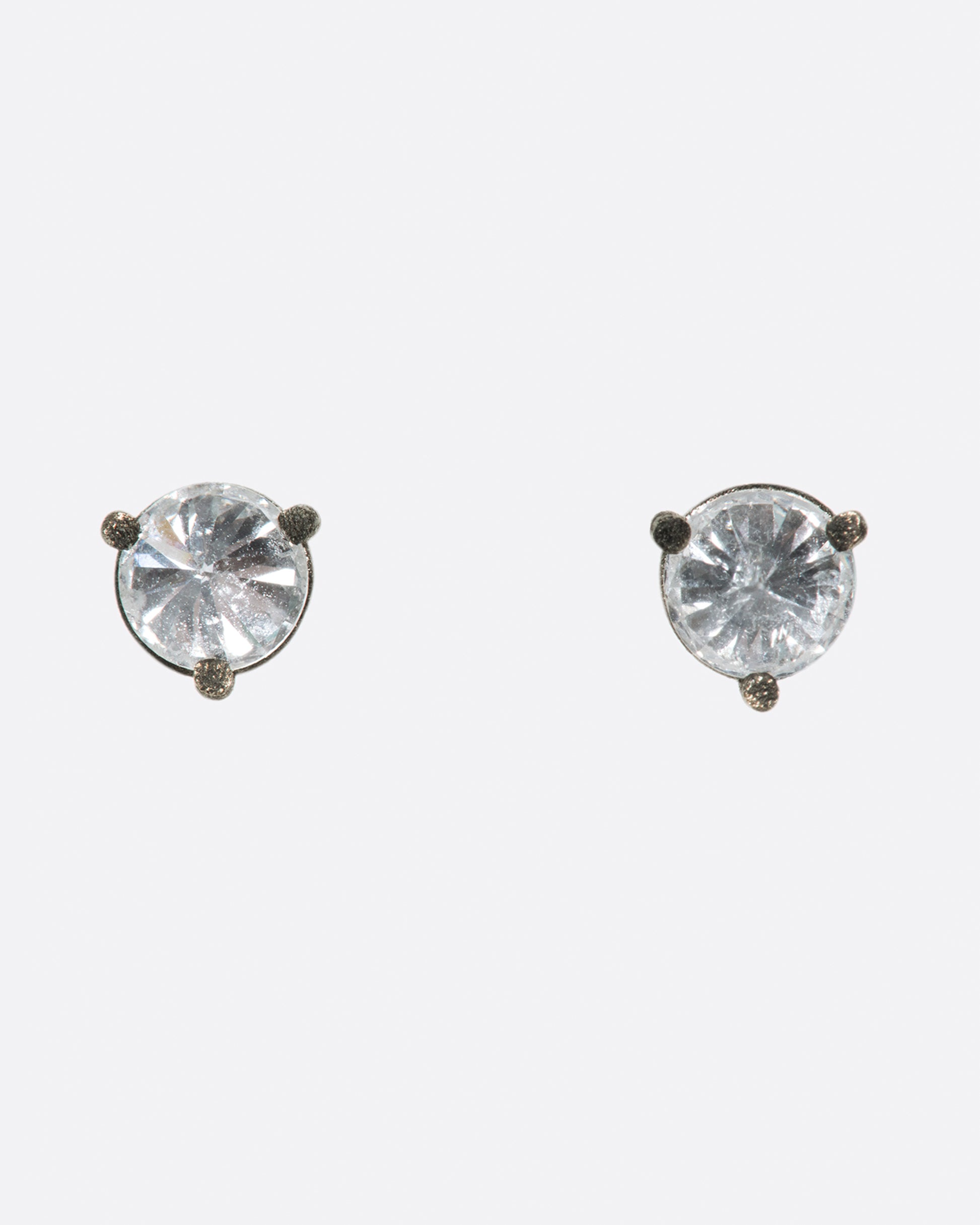 A pair of solitaire stud earrings with round inverted diamonds set in darkened white gold settings.
