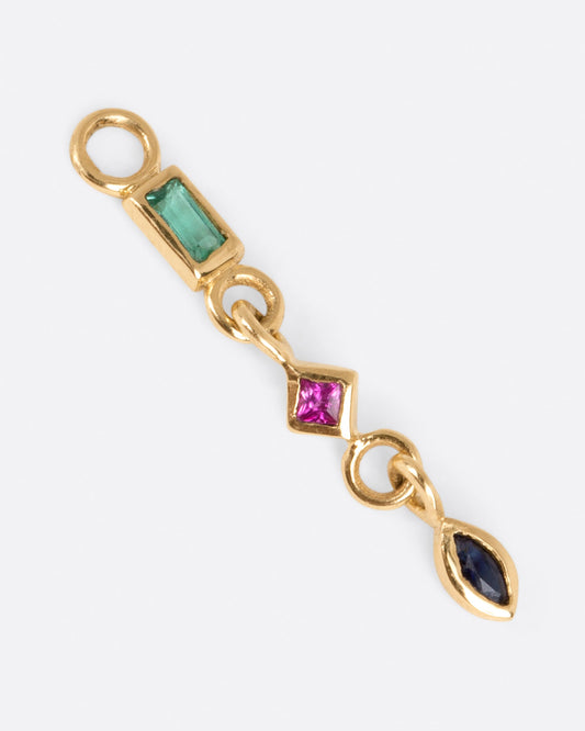 A yellow gold earring dangle with an emerald baguette, princess cut ruby, and marquis sapphire, shown from above.