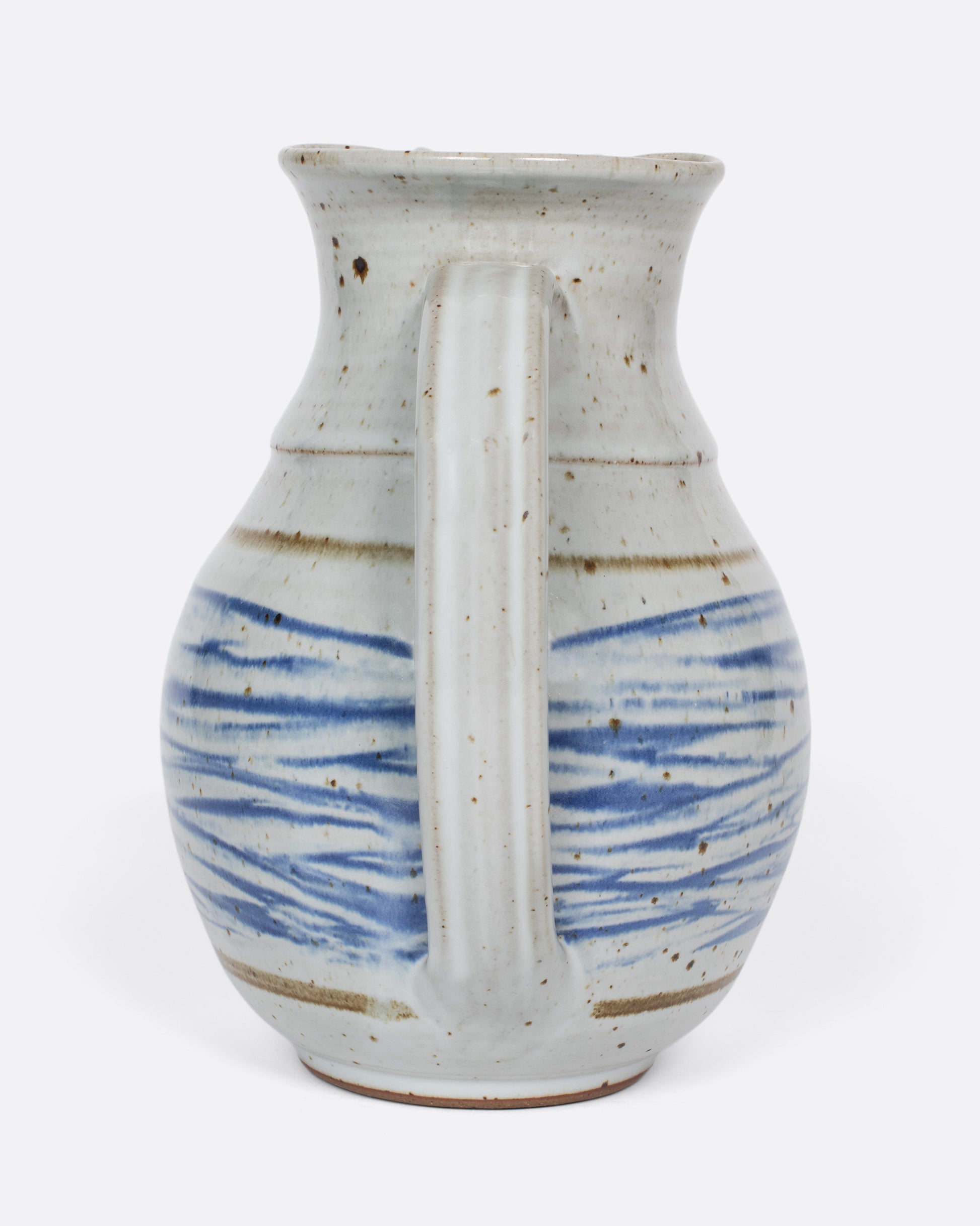 This vintage studio-made ceramic pitcher features a speckled white glaze and a blue water-like, hand-painted pattern.