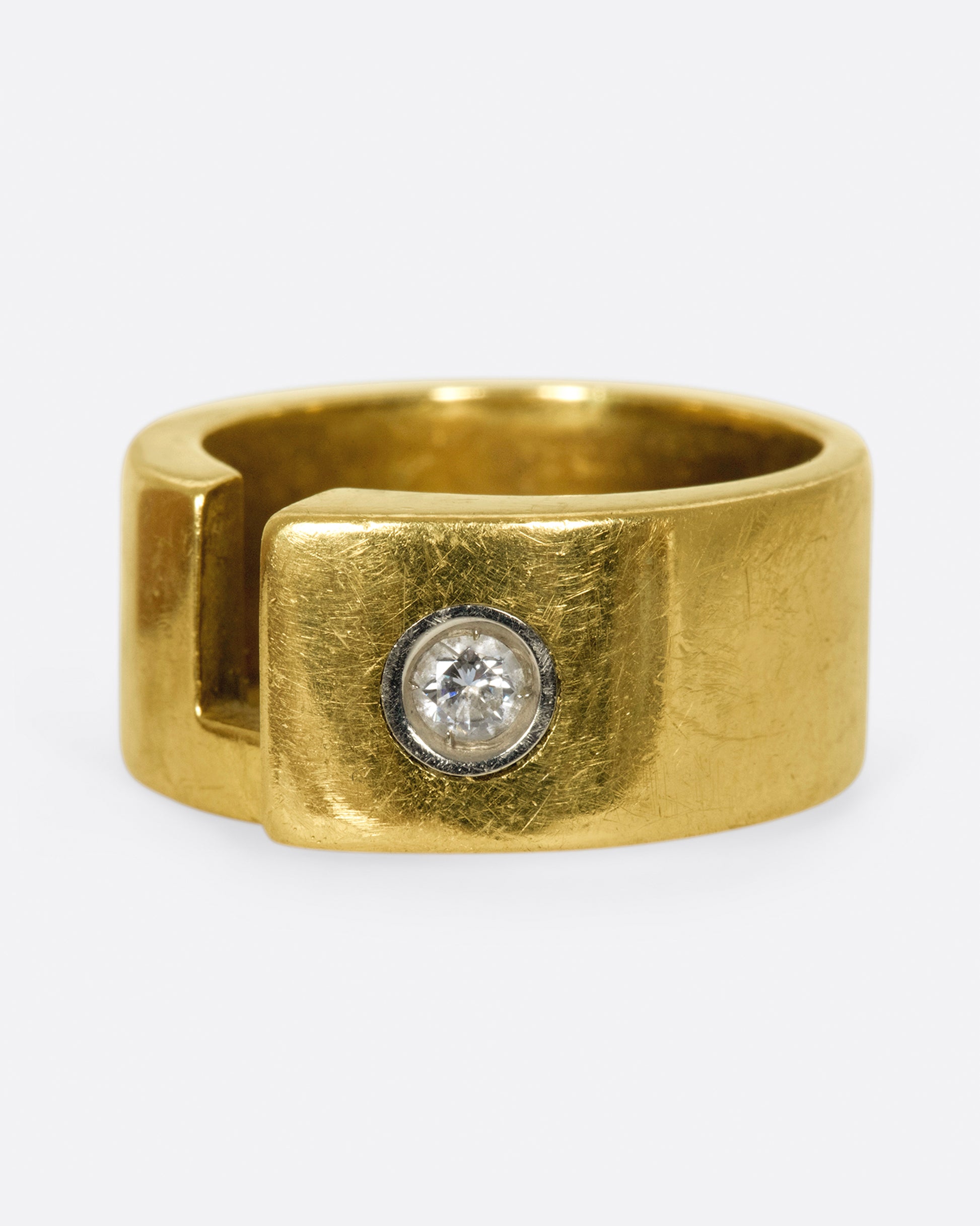 A gold band with a round diamond and rectangular cutout.