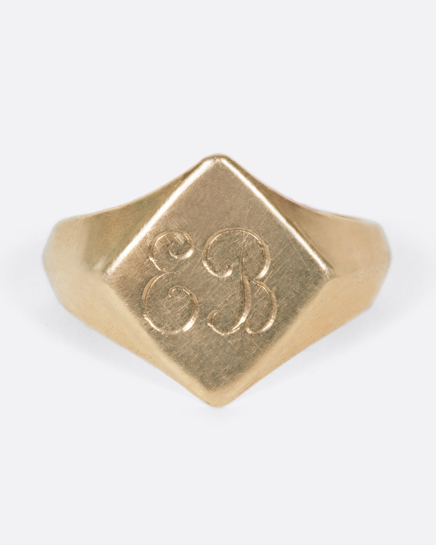 A vintage yellow gold signet ring with a diamond shaped face and the initials EB engraved on the front.