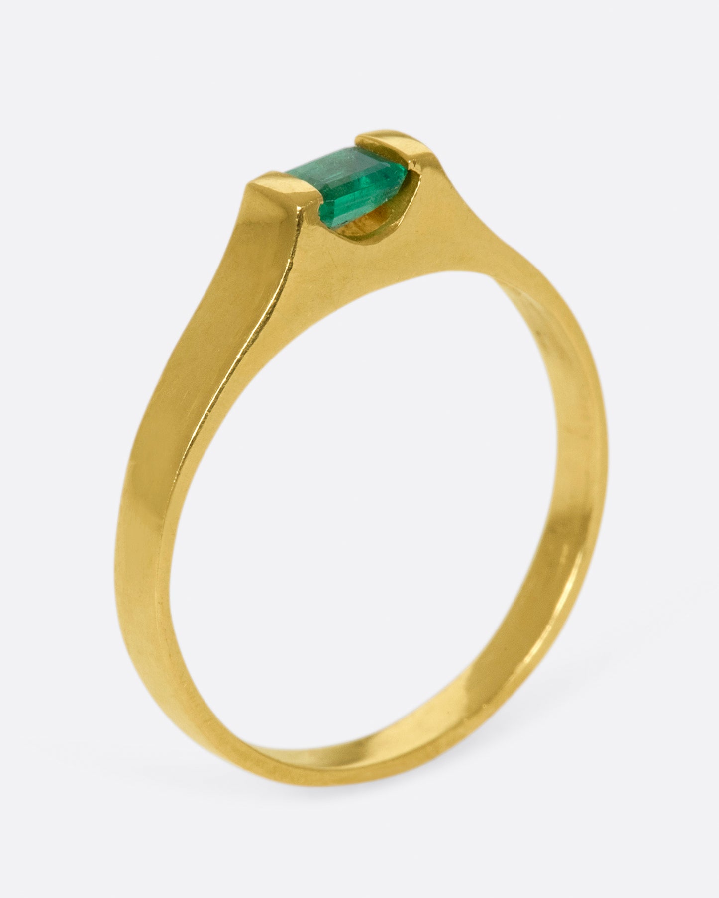 A gold solitaire ring with a tension set emerald cut emerald.