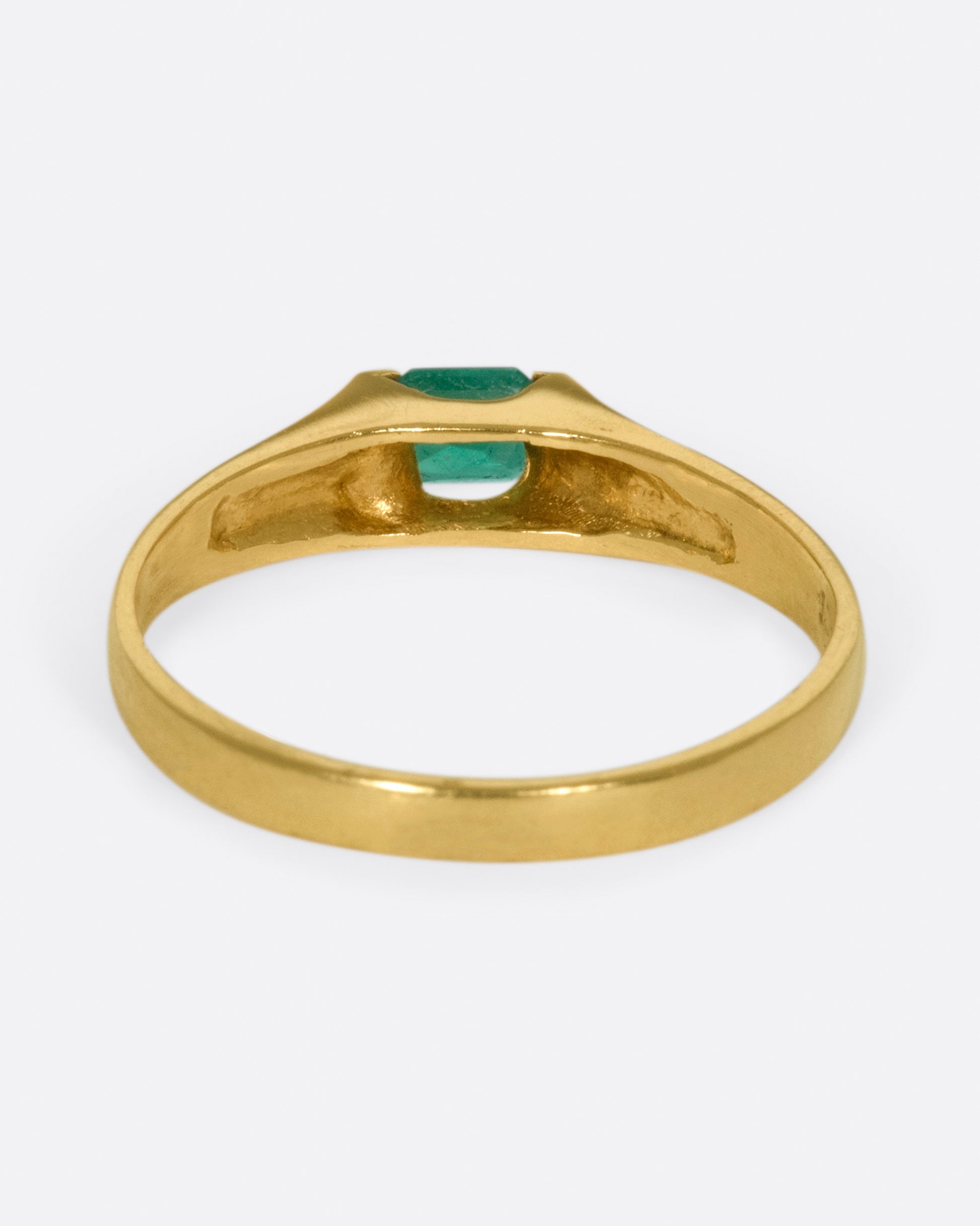 A gold solitaire ring with a tension set emerald cut emerald.