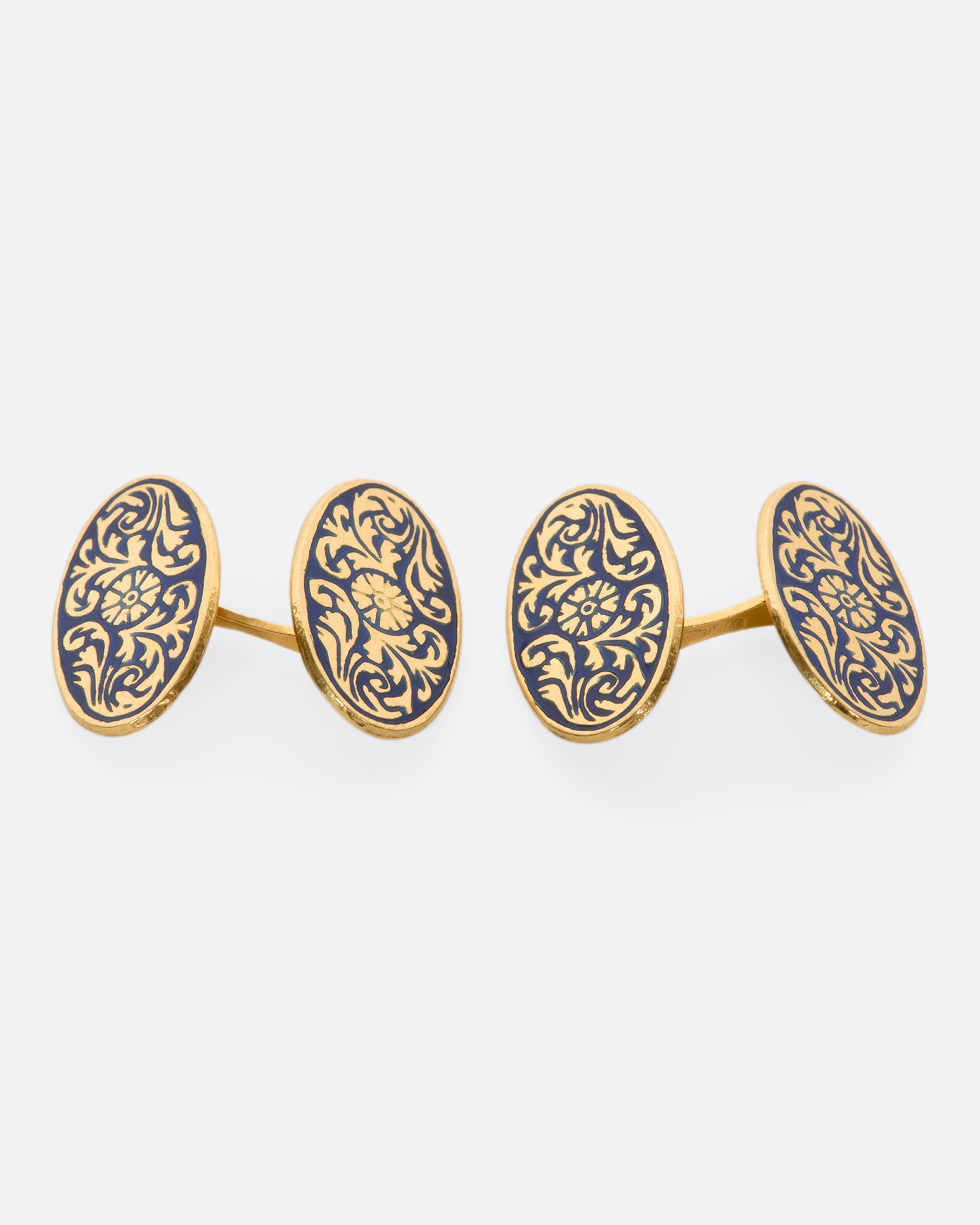 A pair of solid gold vintage cufflinks with intricate flourishes and contrasting dark blue enamel.