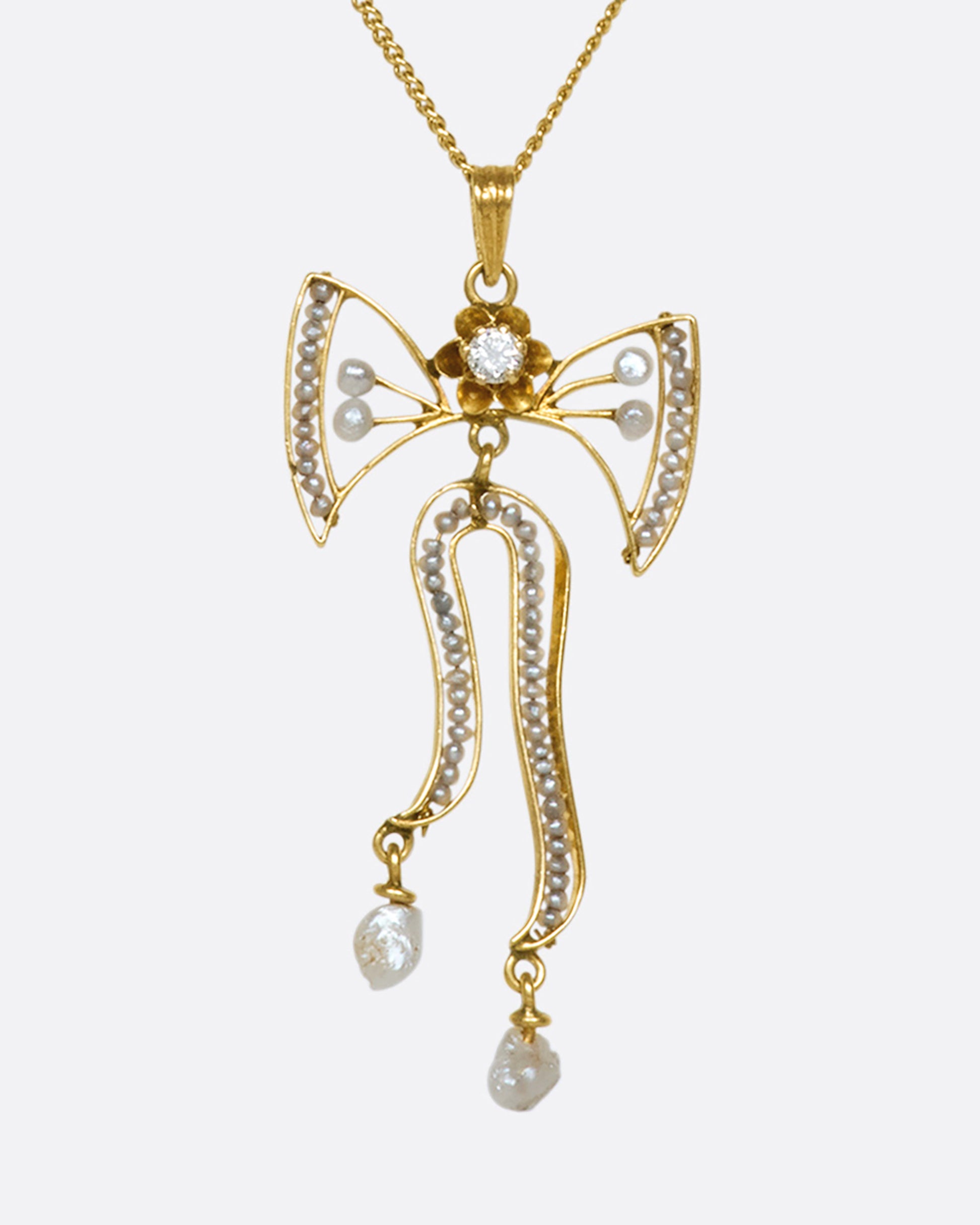 A precious 14k gold bow pendant with diamonds and seed pearls on a 10k gold chain.