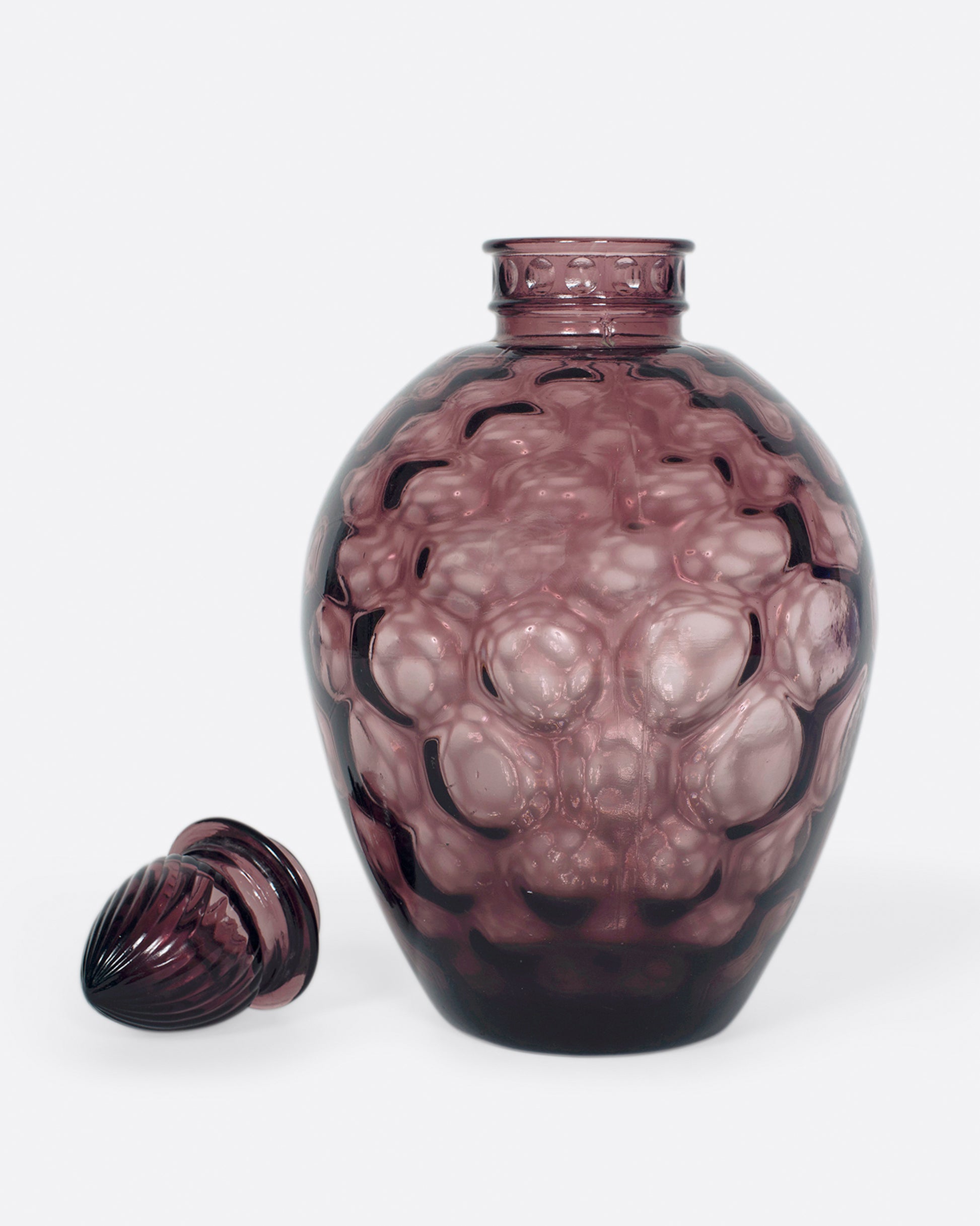 A dark plum, bubble glass bottle with an acorn-shaped stopper.