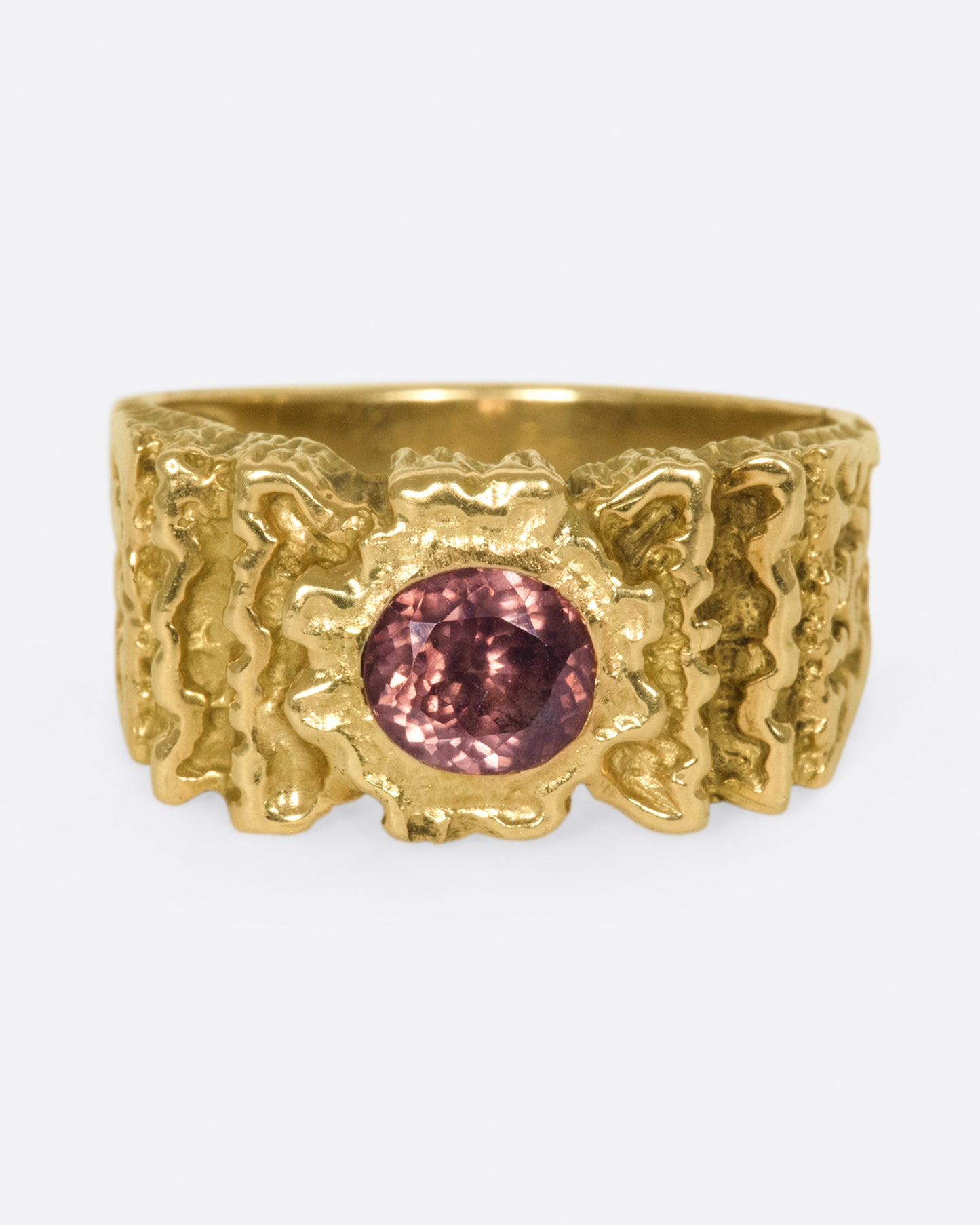 A front view of a yellow gold ring with ribbon texture and round pink spinel.