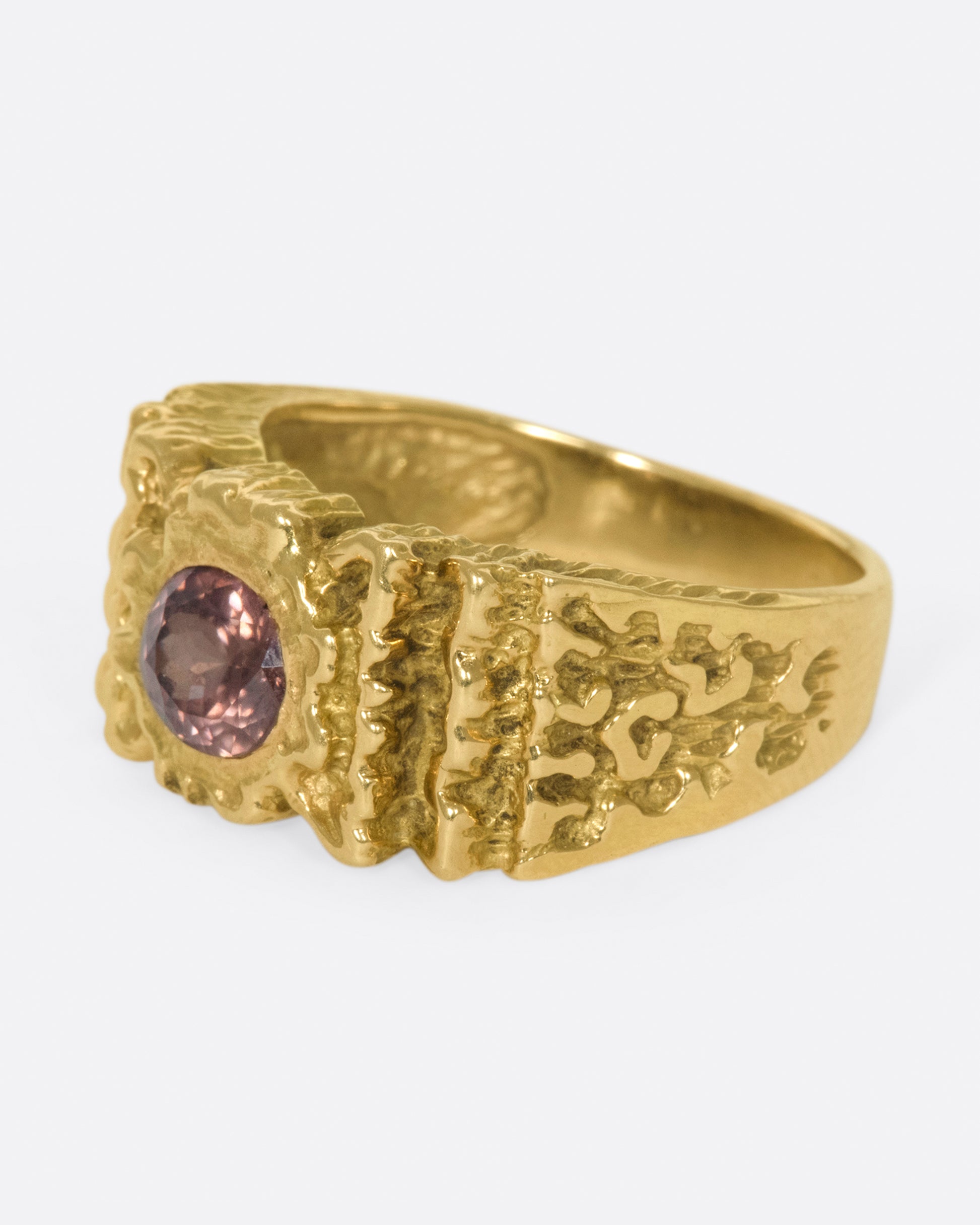 A left side view of a yellow gold ring with ribbon texture and round pink spinel.