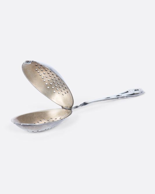 A perforated sterling silver spoon with a detailed cutout handle and a hinged perforated lid to create a tea diffuser.
