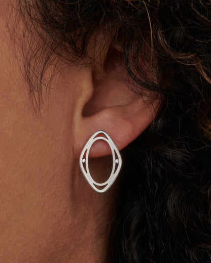 Vintage window stud earring in 18k white gold worn on an ear, an open marquise-shaped frame with a small diamond on each side