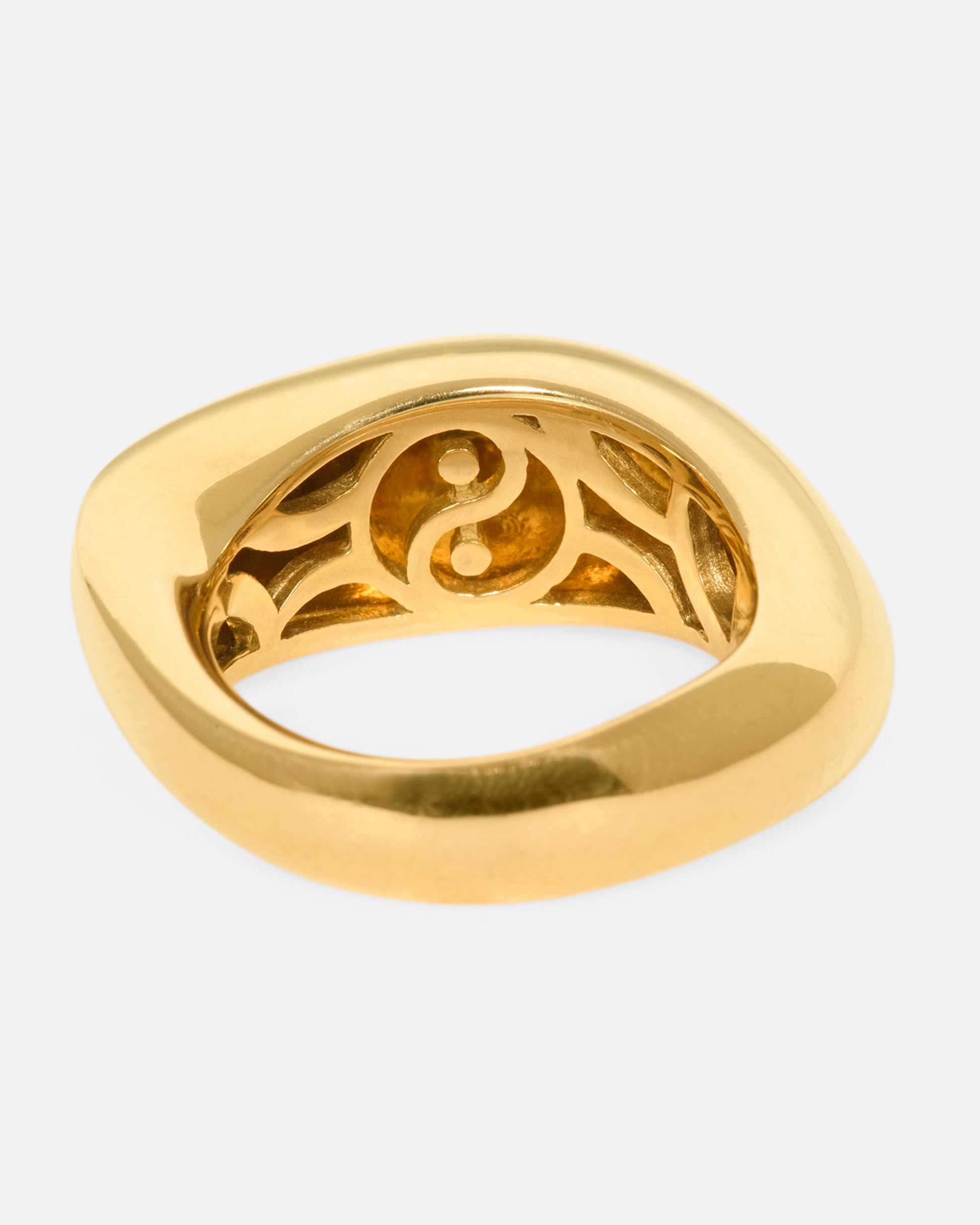 An abstract shaped gold ring with a yin yang symbol cutout on the inside of the band.