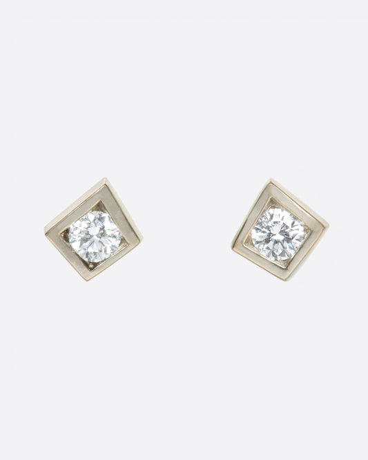 A pair of round diamond solitaire earrings with square tension settings.