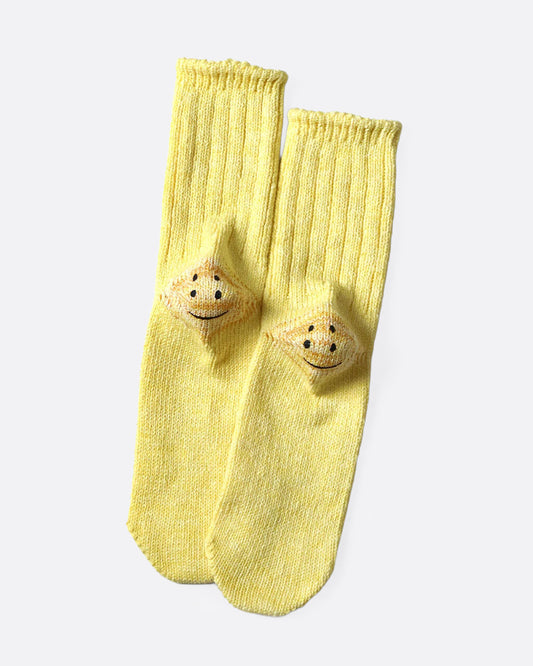 A pair of yellow ribbed cotton socks with double-eyed smiley faces on each heel, shown from the bottom.