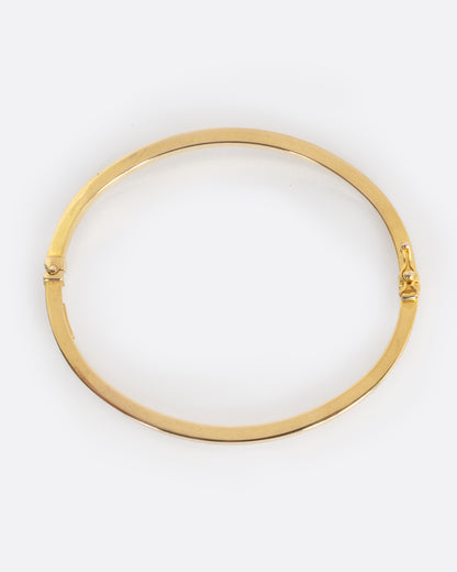 A yellow gold oval hinged bangle with a security clasp, shown from from above laying flat.