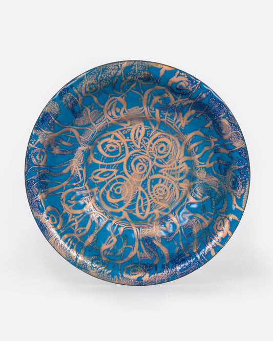A blue enamel plate with a network of gold swirls, shown from the top.