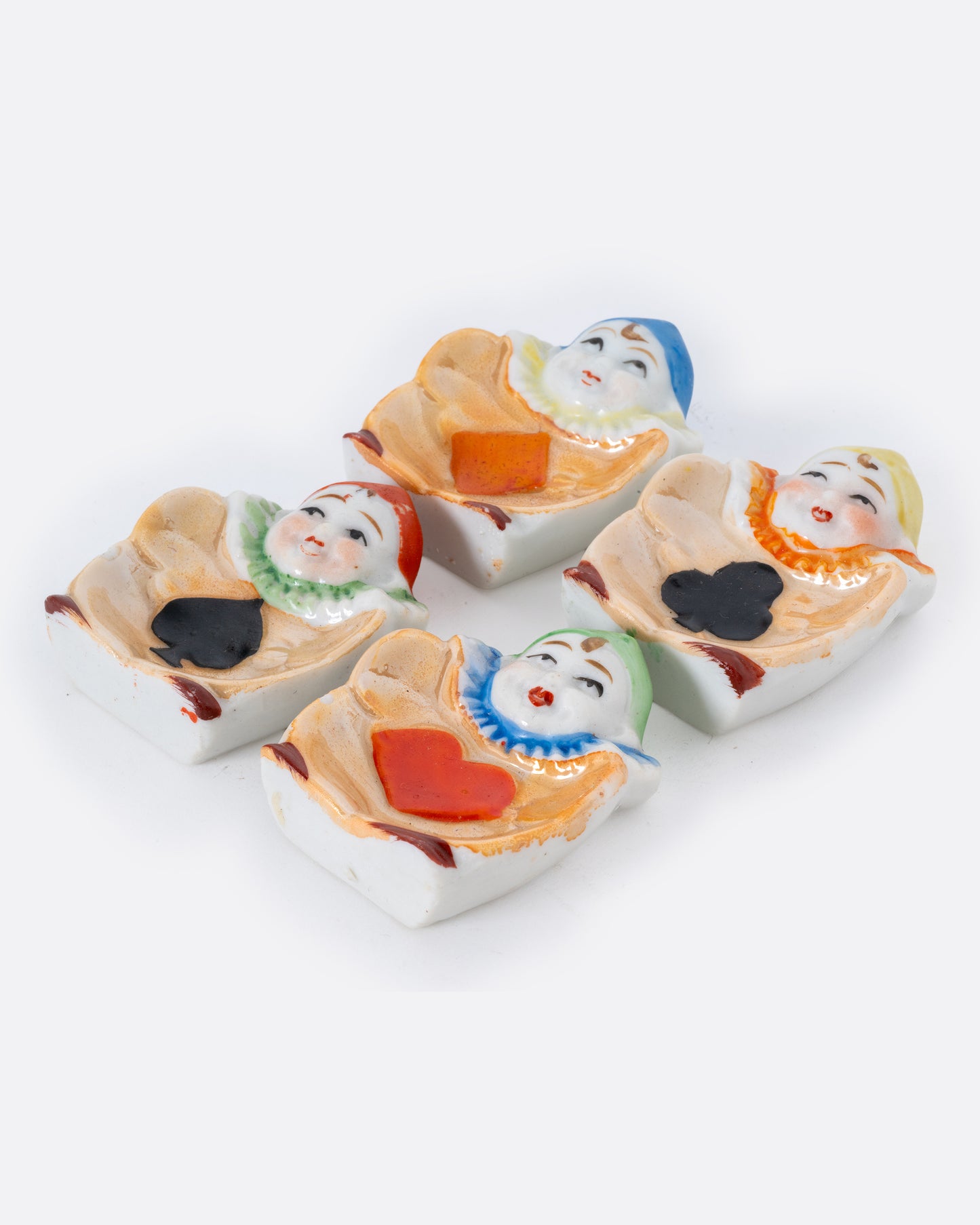 A set of 1940's Japanese harlequin clown dishes with card suit costumes. Shown at an angle from the top.
