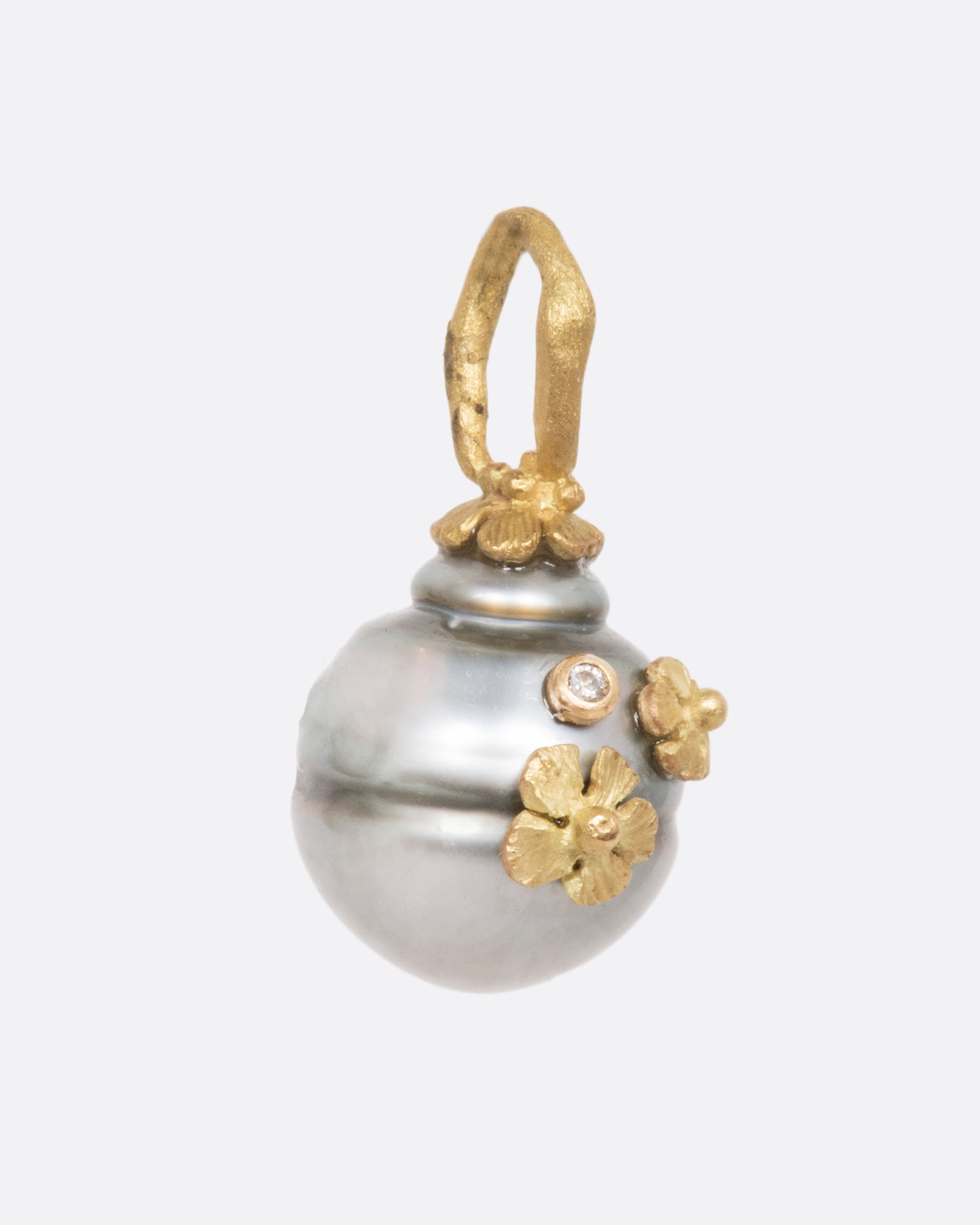 A pearl pendant with a yellow gold bale, adorned with tiny flowers and a diamond. View from the side.