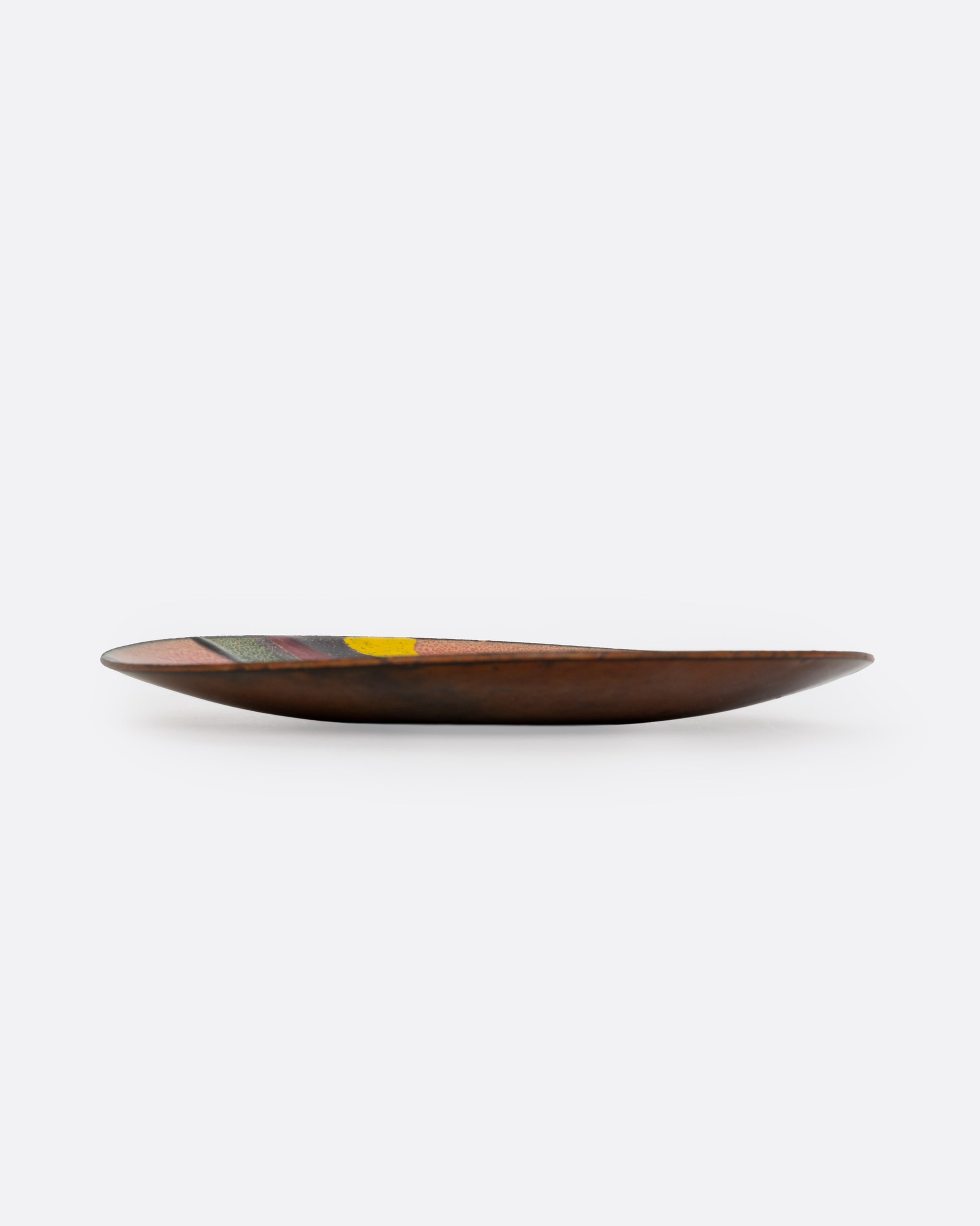 A metal and enamel plate with an abstract graphic design in orange purple, green, and yellow. Shown from the side.
