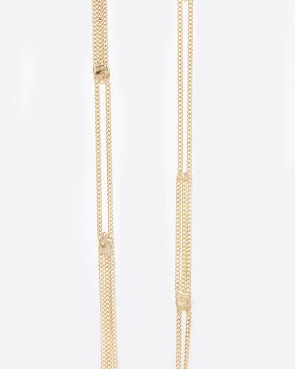 A long yellow gold multi chain necklace with alternating pattern of squares finished with gold solder. Shown close up from the front.