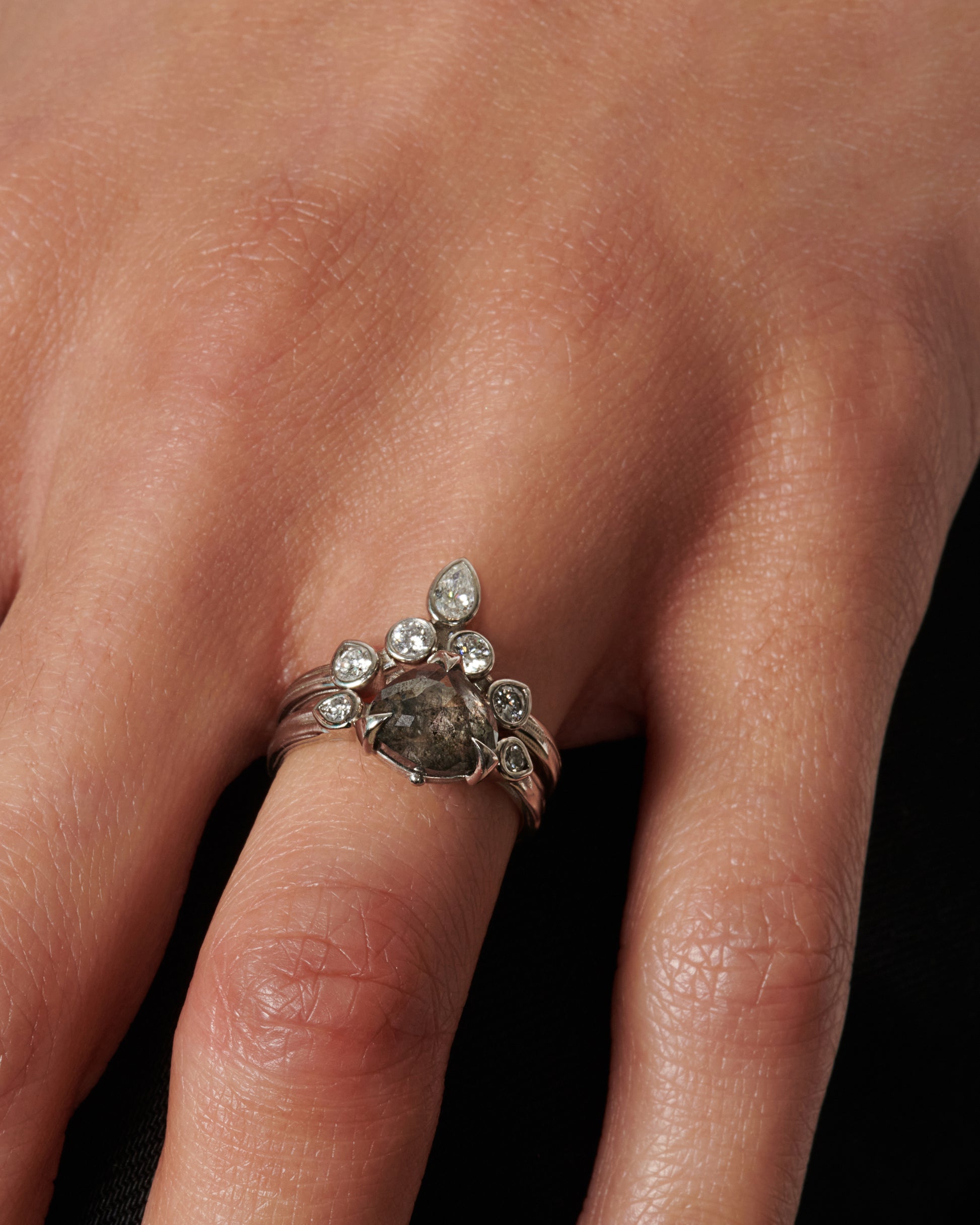 A dark, glamorous ring with a rose cut, heart-shaped grey diamond embraced in pointed claw settings and surrounded by round white diamond accents.