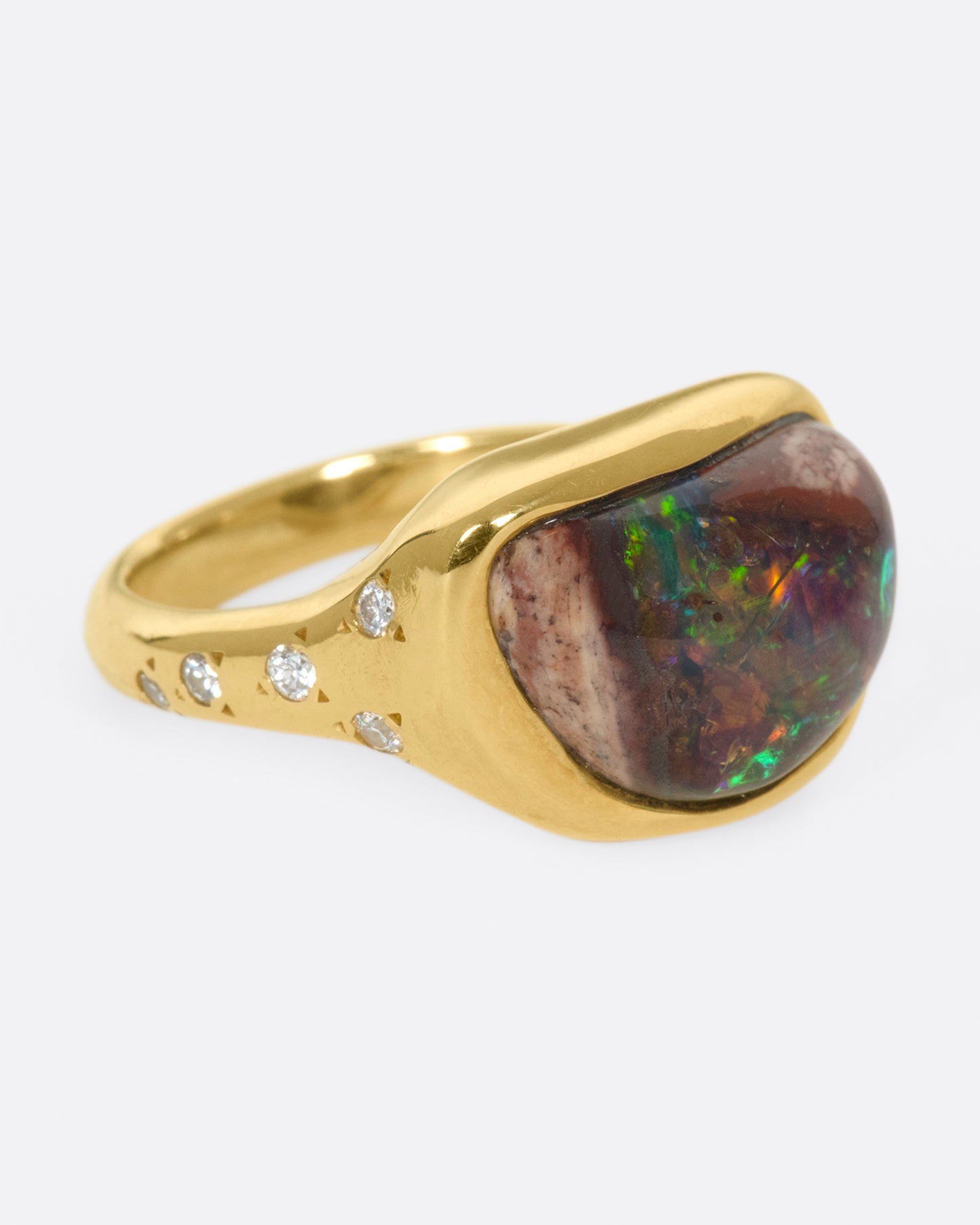 A gold ring with a bezel set curved black opal and round diamond accents.