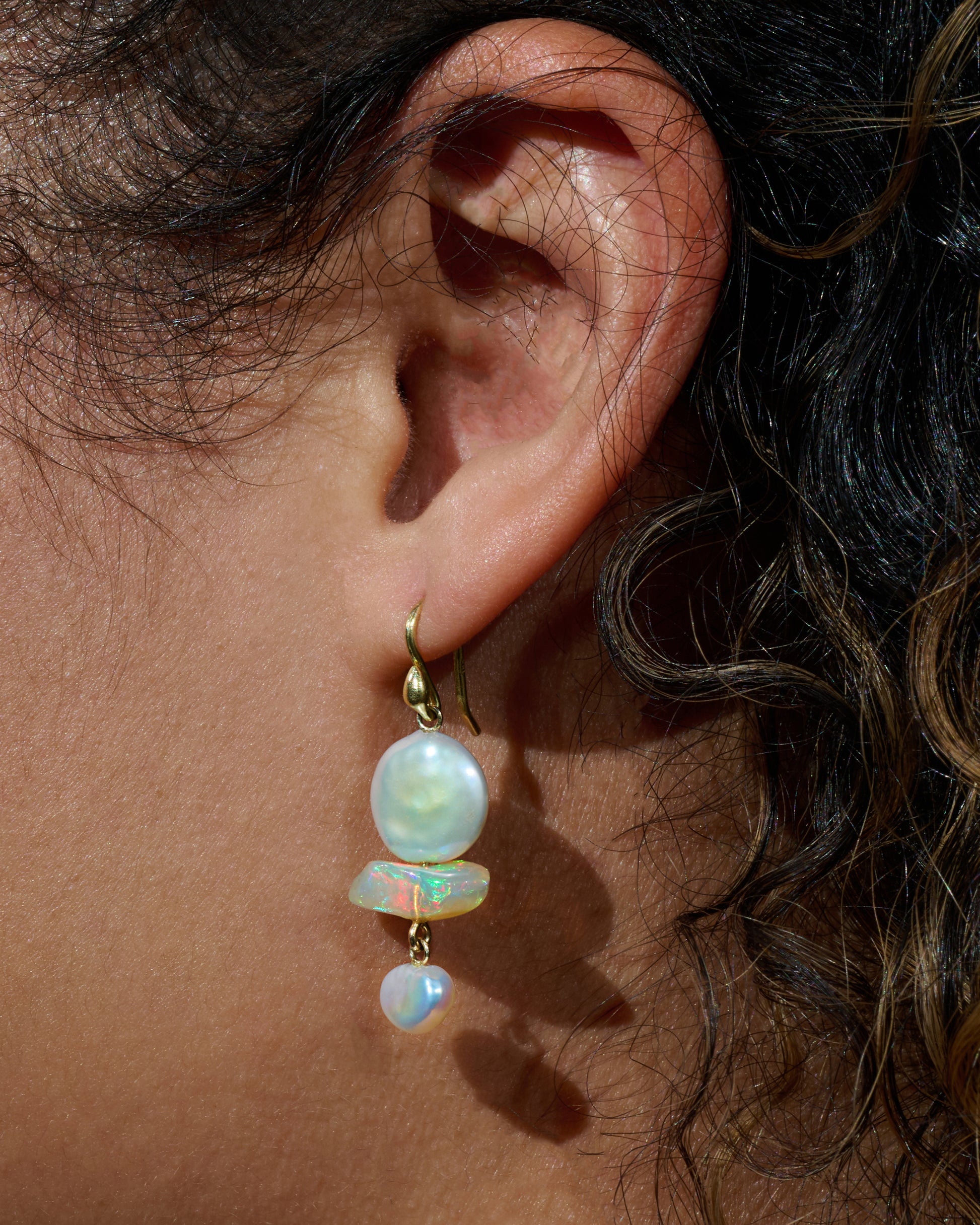 Yellow gold triple tier drop earrings with pearls and opals. View on an ear.