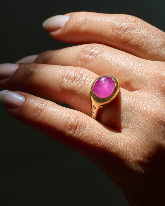 A yellow gold signet ring with a ruby cabochon and diamonds on either shoulder. Shown from the side ob a person.