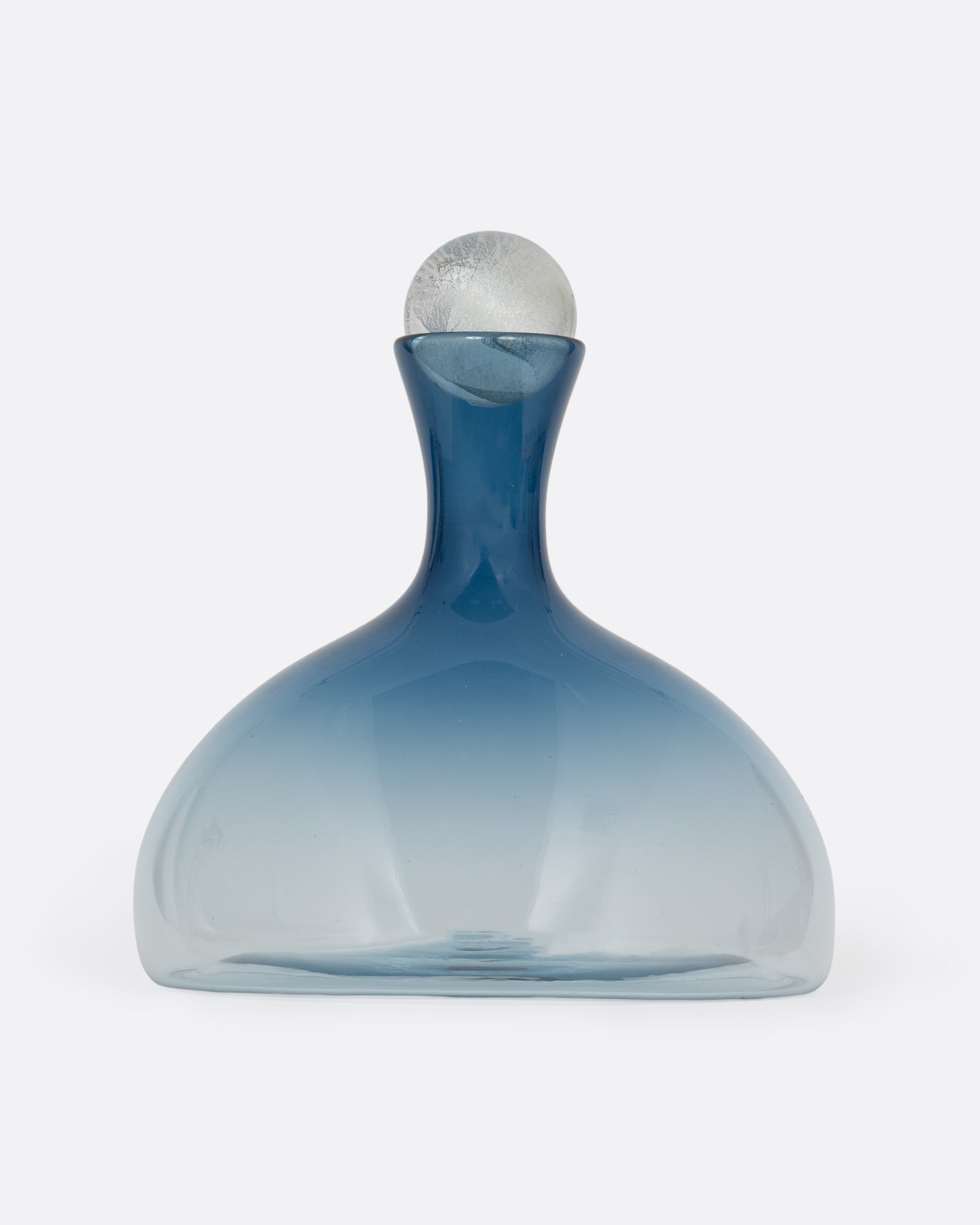 A blown glass decanter in a steel blue gradient with a wide base and a round silver stopper, shown from the front.