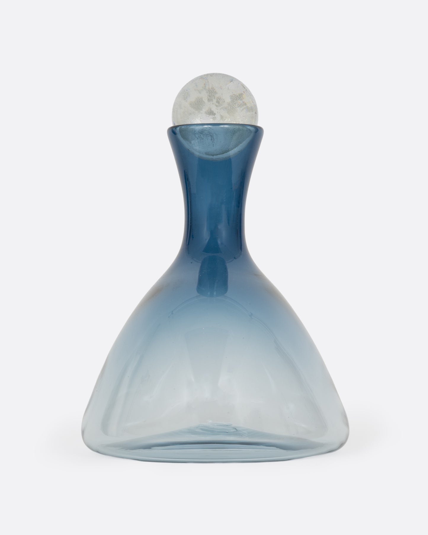 A blown glass decanter in a steel blue gradient with a wide base and a round silver stopper, shown from the side.