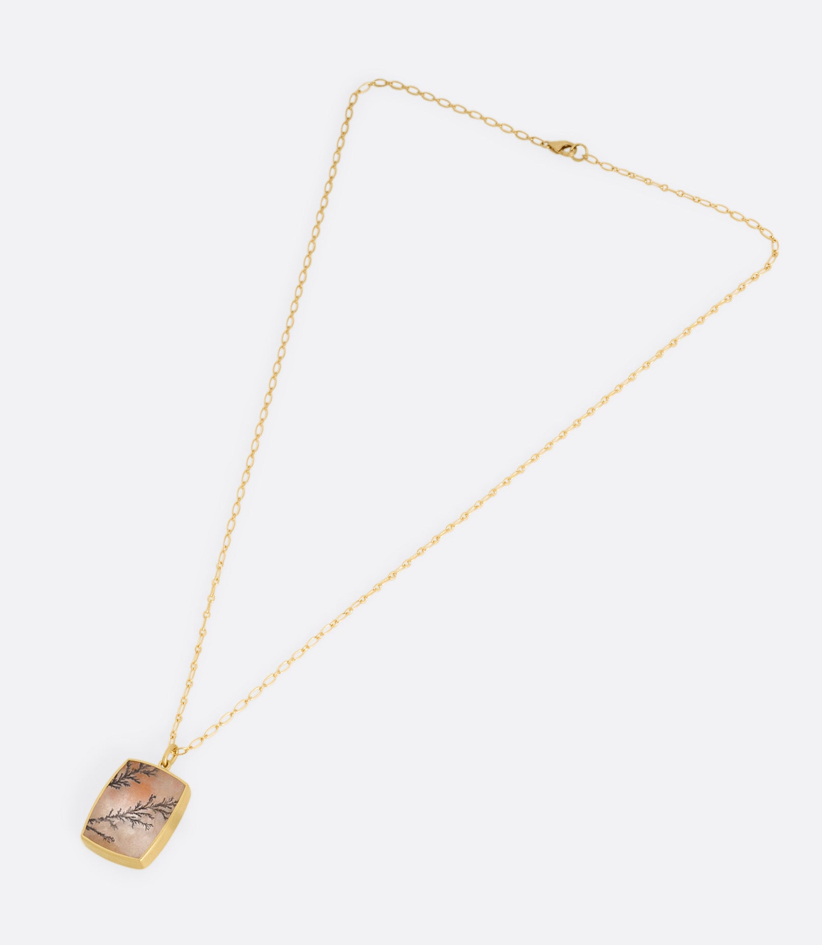 A yellow gold dendritic quartz pendant hanging from an alternating oval chain. Shown laying flat.
