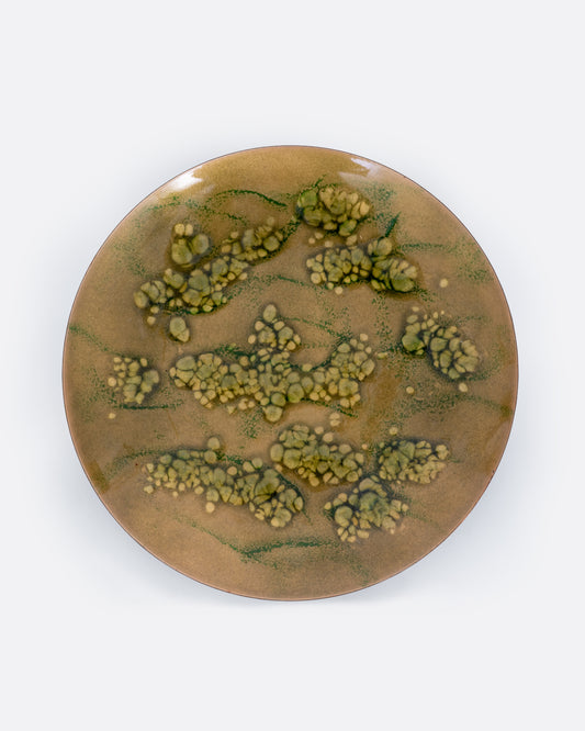 A metal and enamel plate with an abstract cluster design in green and yellow. Shown from the top.